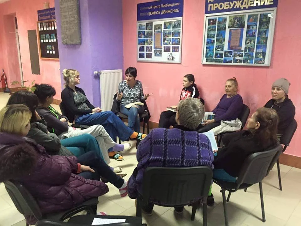 A group of four young women sitting at a table in a café or restaurant, engaging with a tablet and smiling.