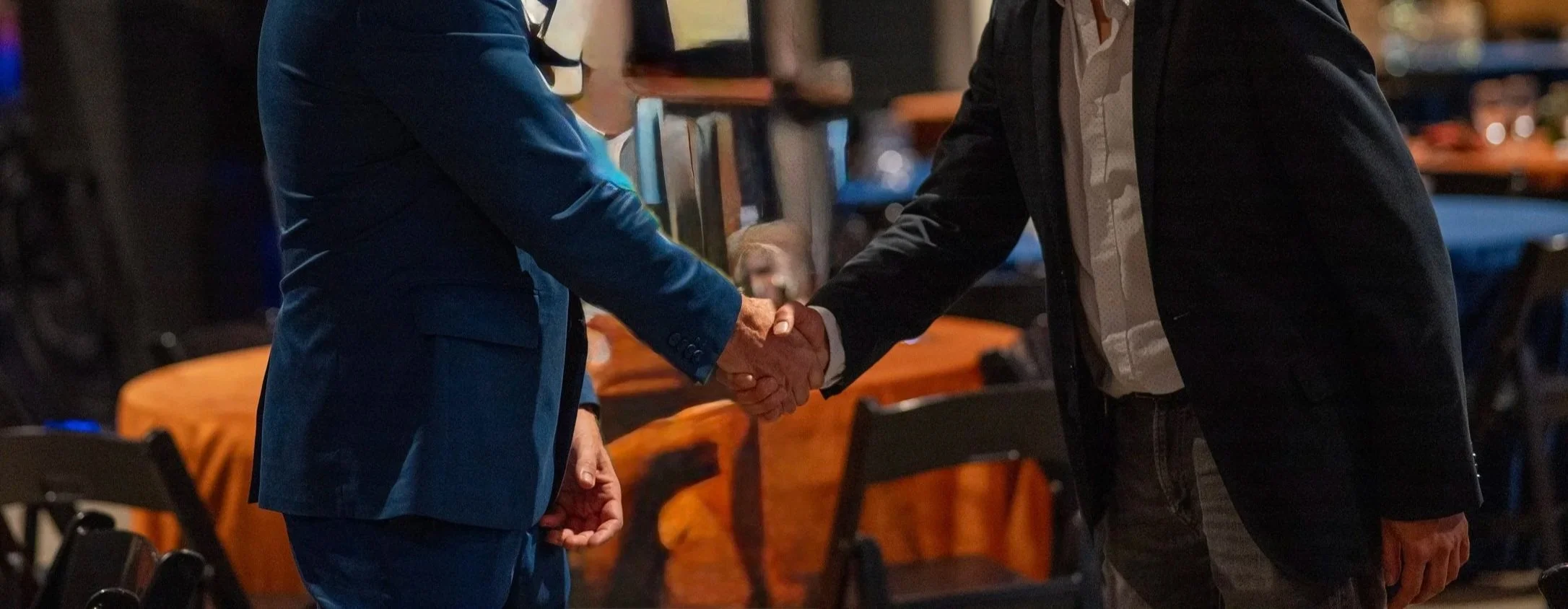 Young man sitting on a bench against a neutral wall, wearing a gray polo shirt and beige pants, with a contemplative expression and shadow cast on the wall.