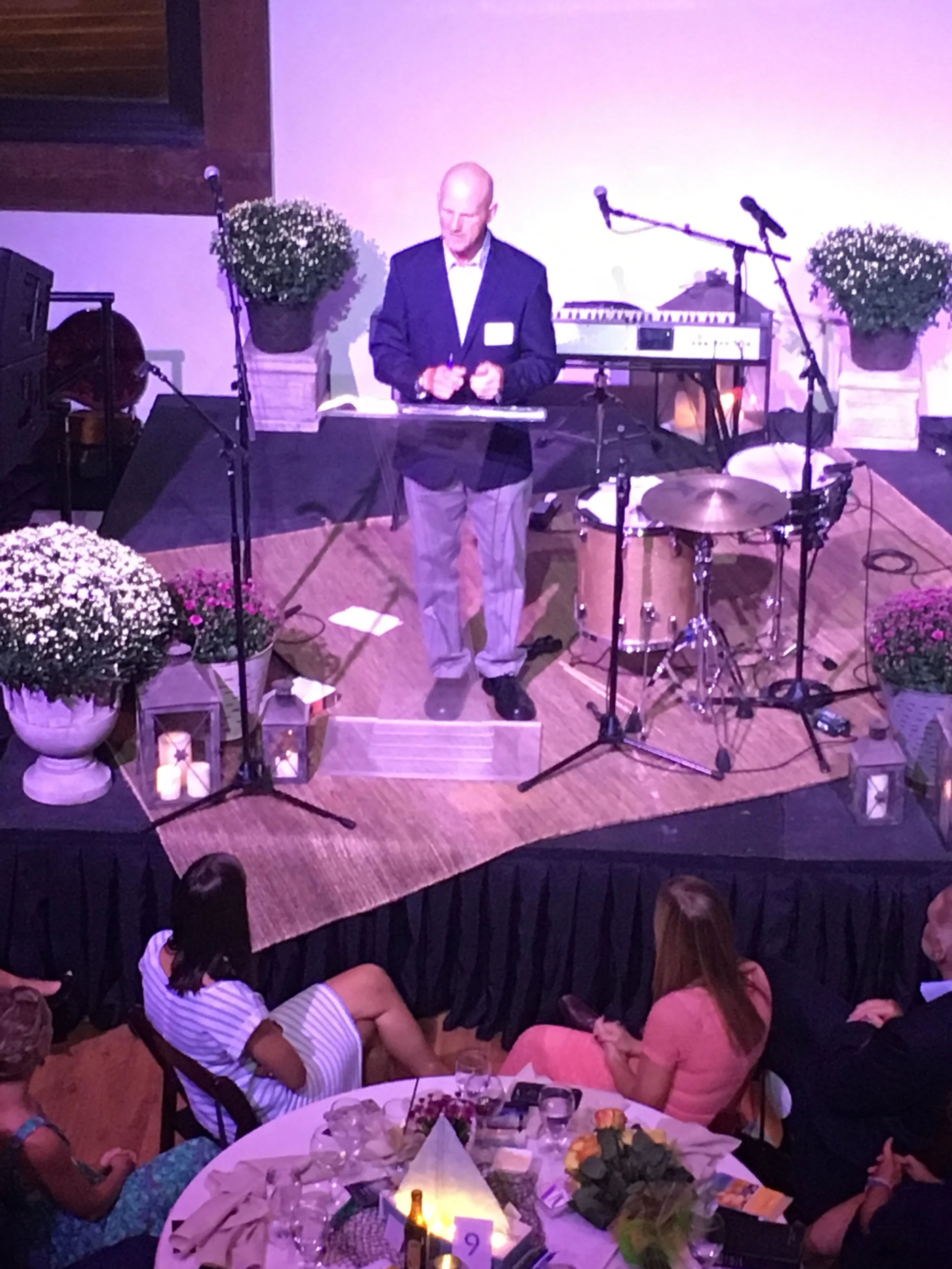 Woman with curly hair sitting on a bench in a room with sunlight, wearing a beige sleeveless top and brown wide-leg pants, with shadows cast on the wall behind her.