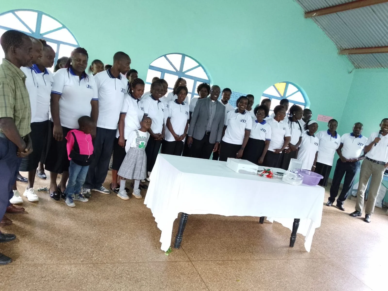 Group of adults and children standing inside a room with blue arched windows, posing for a photo around a table.