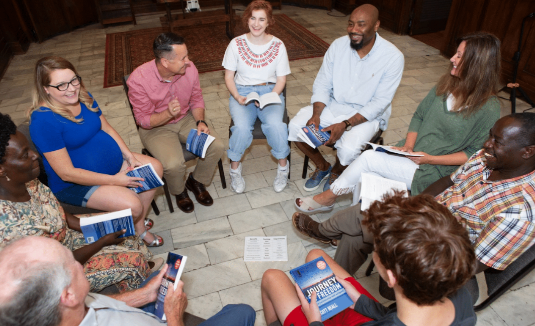 A group of four young women sitting at a table in a café or restaurant, engaging with a tablet and smiling.