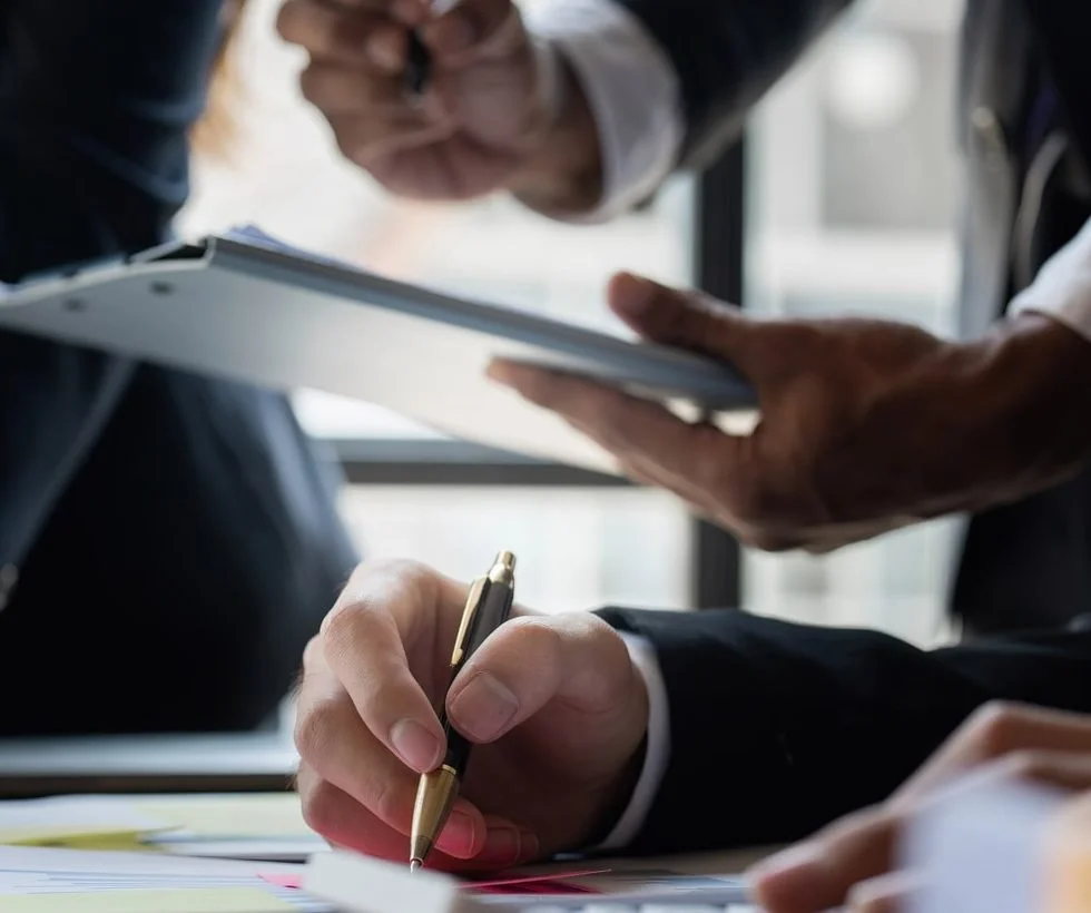 Close-up of hands in business attire, one holding a pen and the other holding a tablet, during a business meeting.