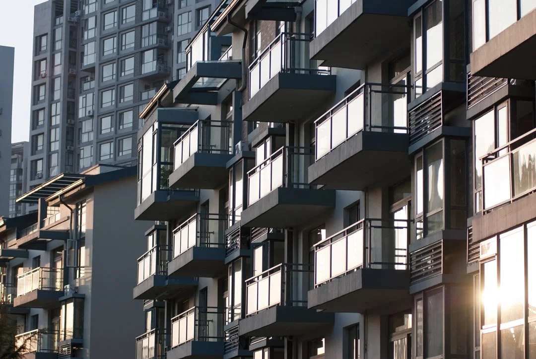 Modern apartment buildings with multiple balconies and glass railings, sunlight reflecting off windows.