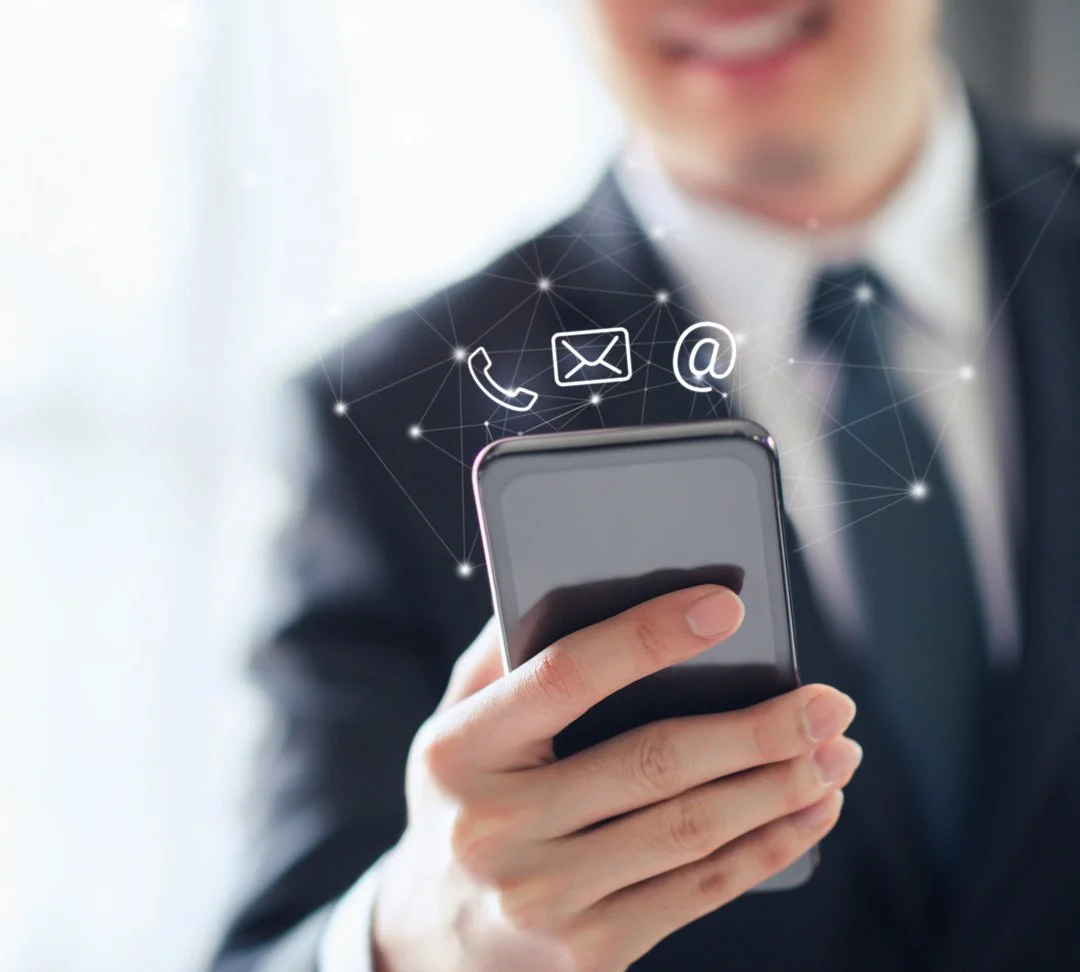 Person in business suit holding smartphone with icons for phone, email, and at sign above it.