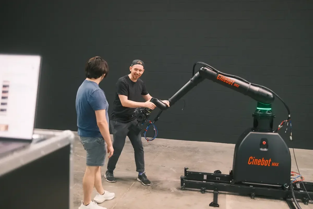 Two crew members beside a Cinebot Max robotic camera arm on studio track