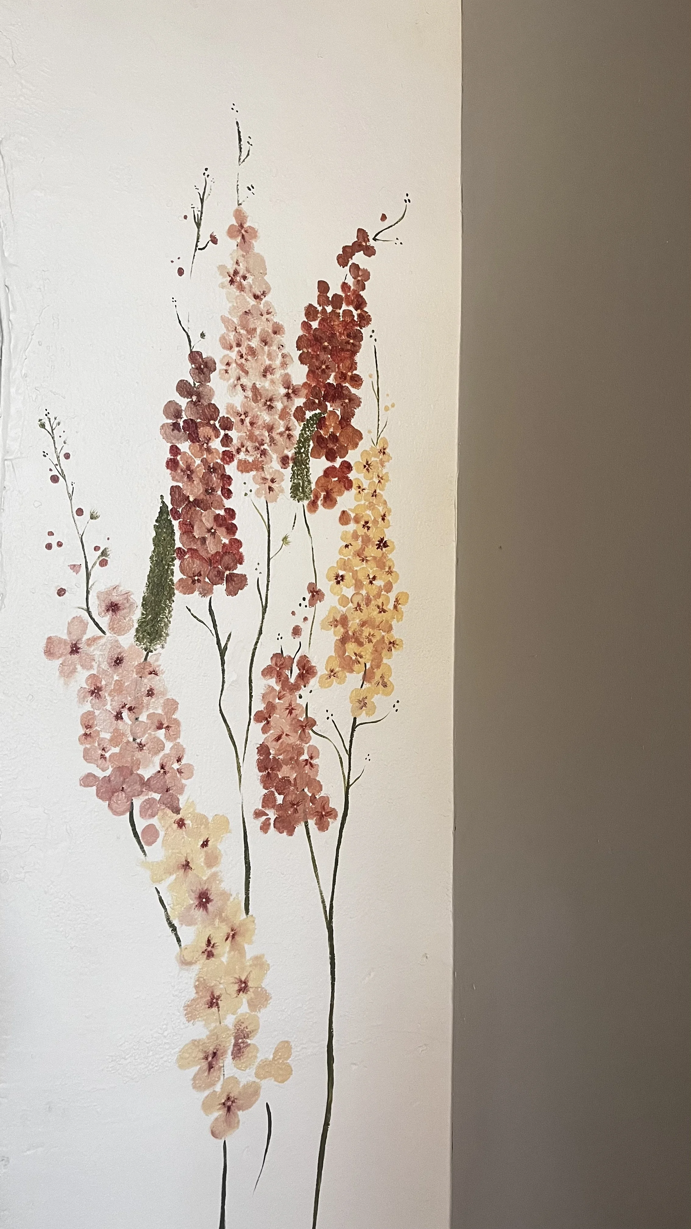 Watercolor painting of pink, red, and yellow flowers on green stems on a white wall.
