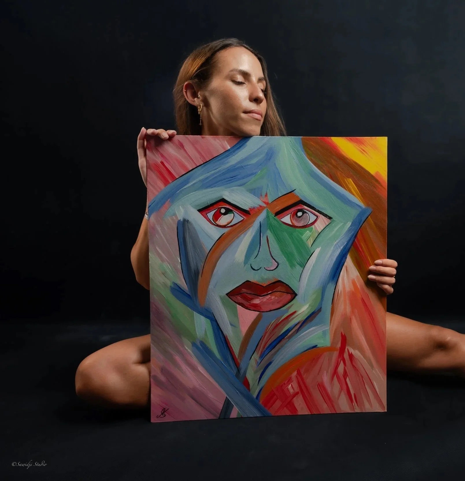 Künstlerin in einem Fotoshooting mit den Werk "Self-Alchemy“ , Augen geschlossen, sinnliche Pose, Bild in der Hand haltend.