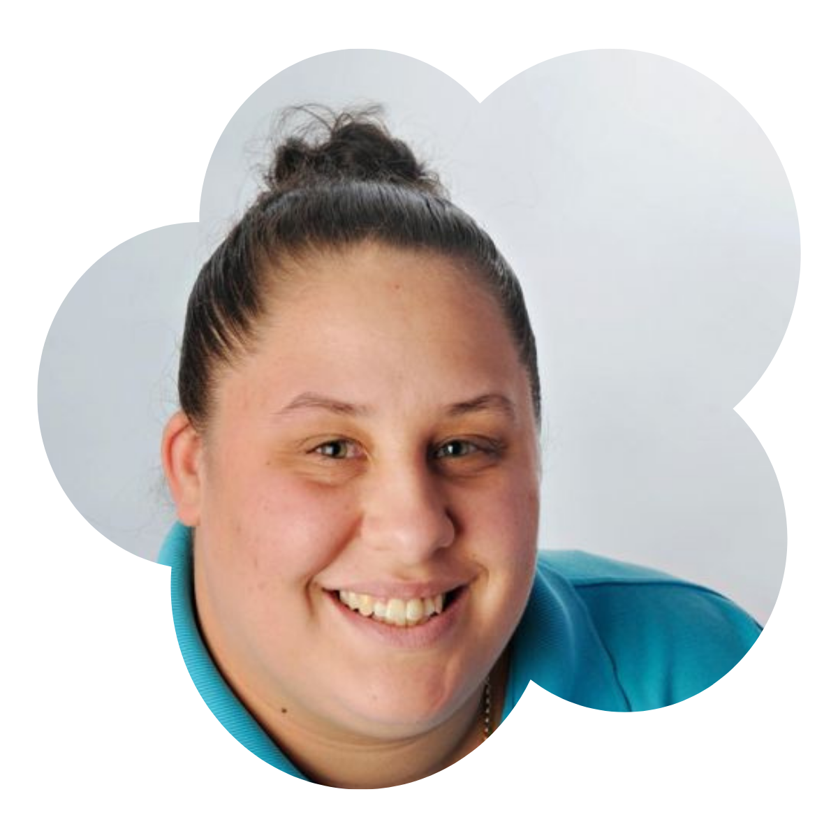 A woman with dark hair in a bun, smiling, wearing a blue collared shirt, against a plain light background.