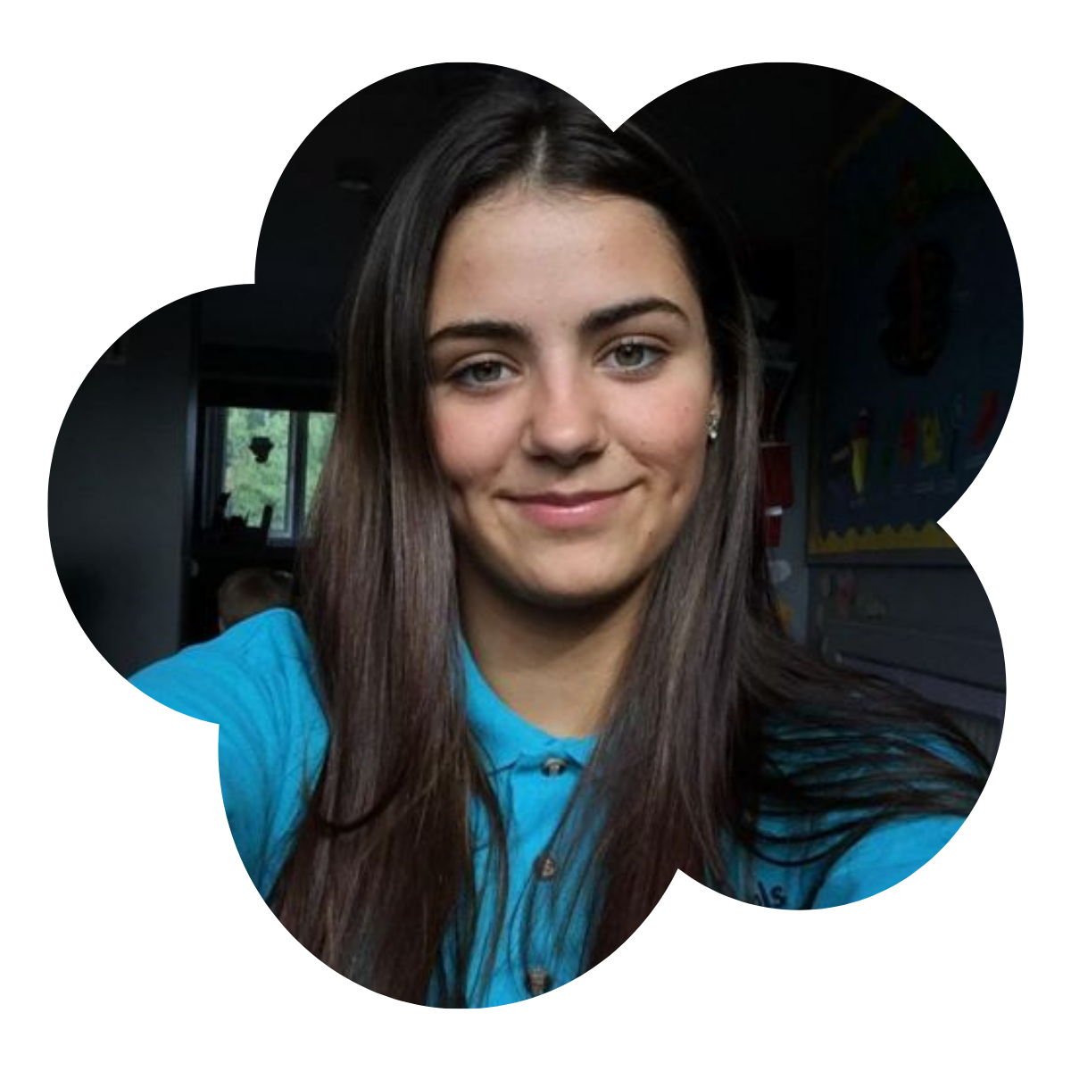 A young woman with long dark hair wearing a blue shirt smiling at the camera indoors.