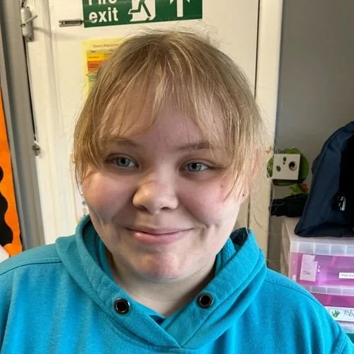 A warm and friendly member of nursery staff smiling in a smart uniform in a bright toddler room in a daycare nursery in Solihull.