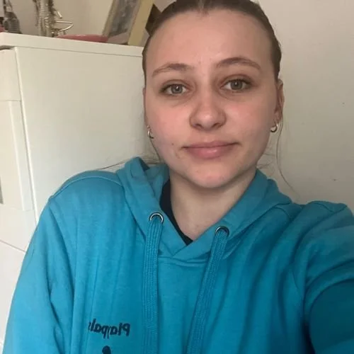 A woman wearing a blue hoodie taking a selfie indoors.