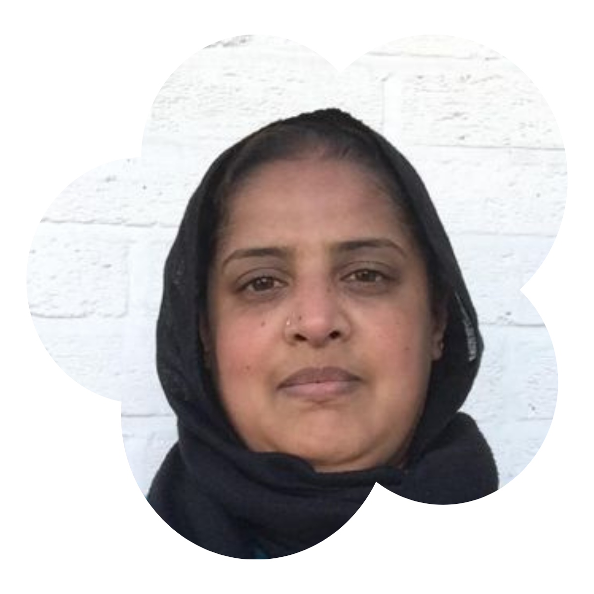 A woman with dark hair and a headscarf standing in front of a white brick wall.