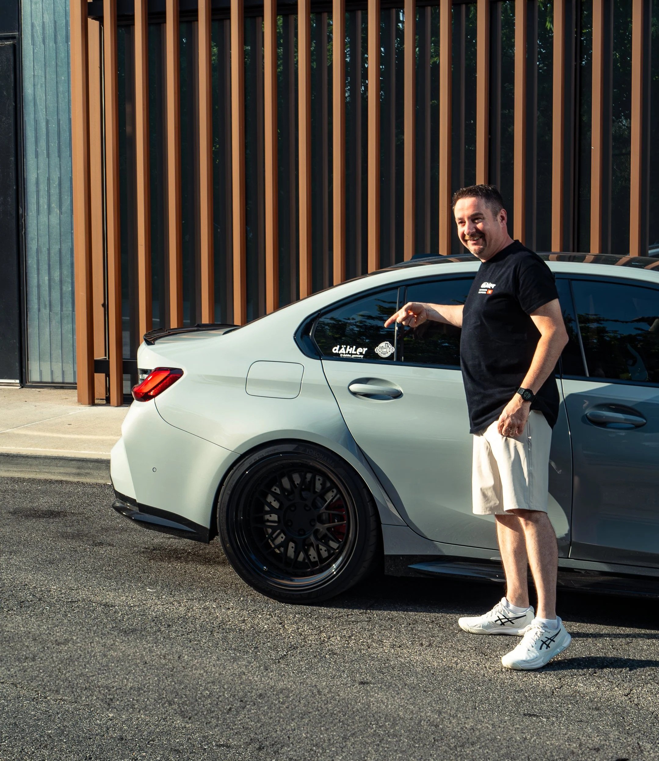 Dahler CEO Jorg Wey standing by a BMW G80 in Brooklyn Gray, pointing at a Dahler logo sticker on the car window.