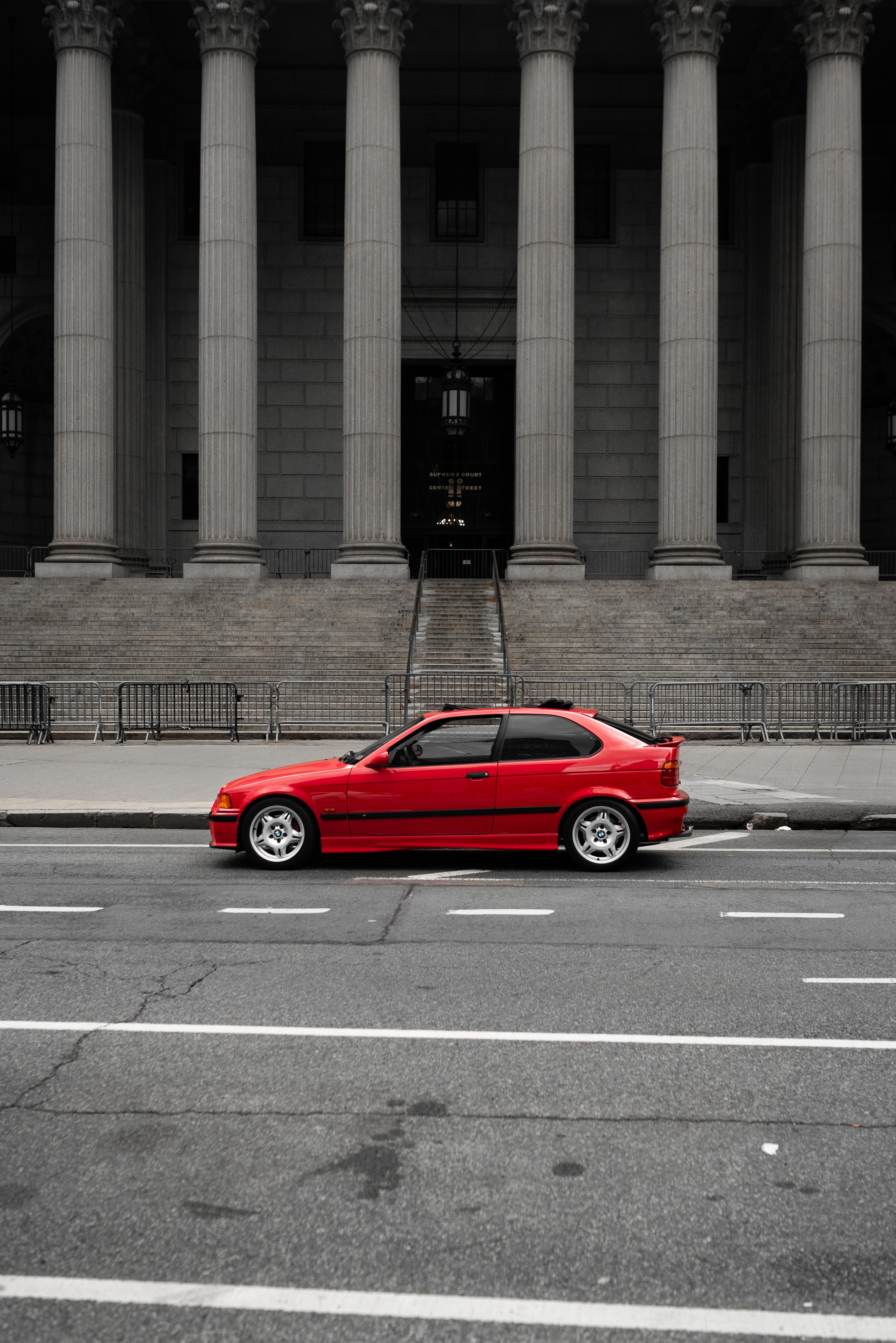 318ti BMW parked in front of a government building with tall concrete columns in New York City.