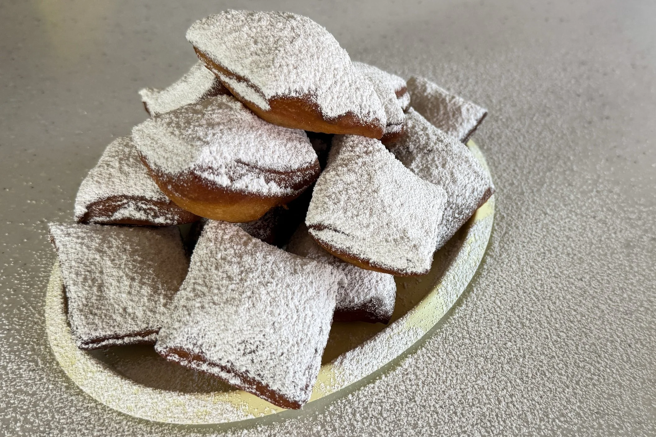 a yellow tray piled with square beignets topped generously with powdered sugar.