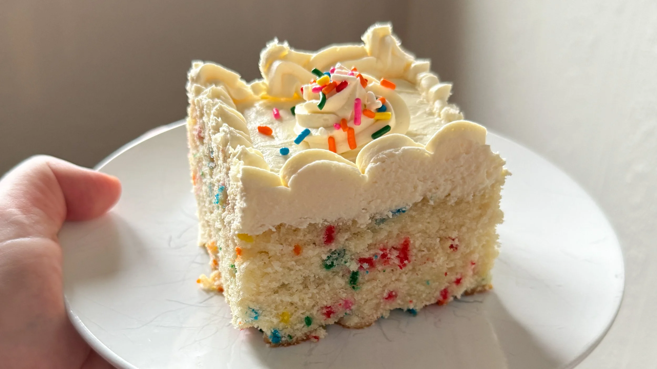 A slice of funfetti sheet cake on A WHITE PLATE.