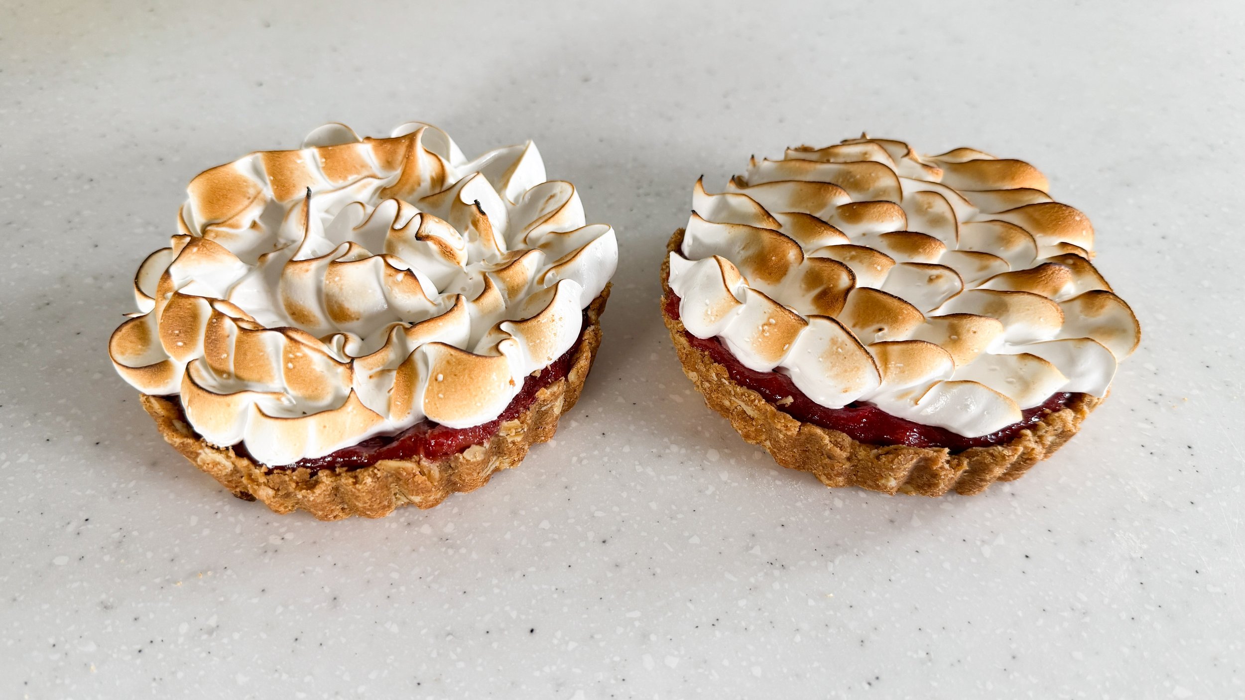 Two rhubarb meringue tartlets on a white platter.