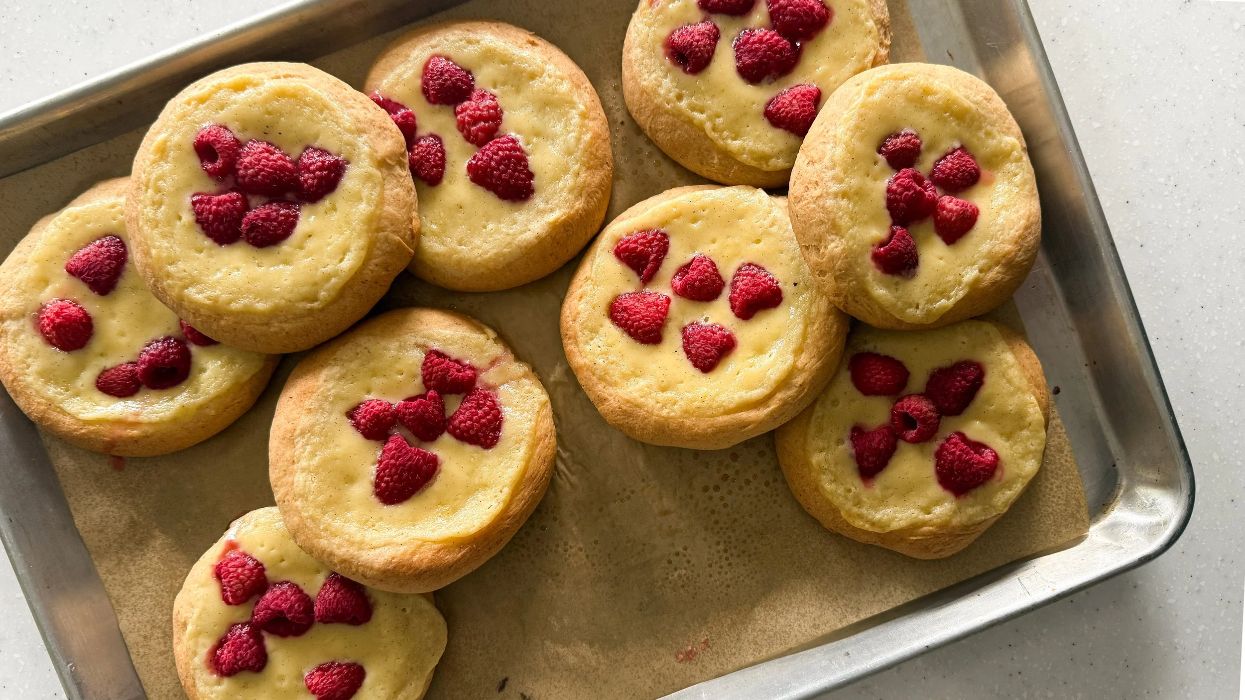 A tray holding lightly browned pastries filled with mascarpone cream and raspberries.