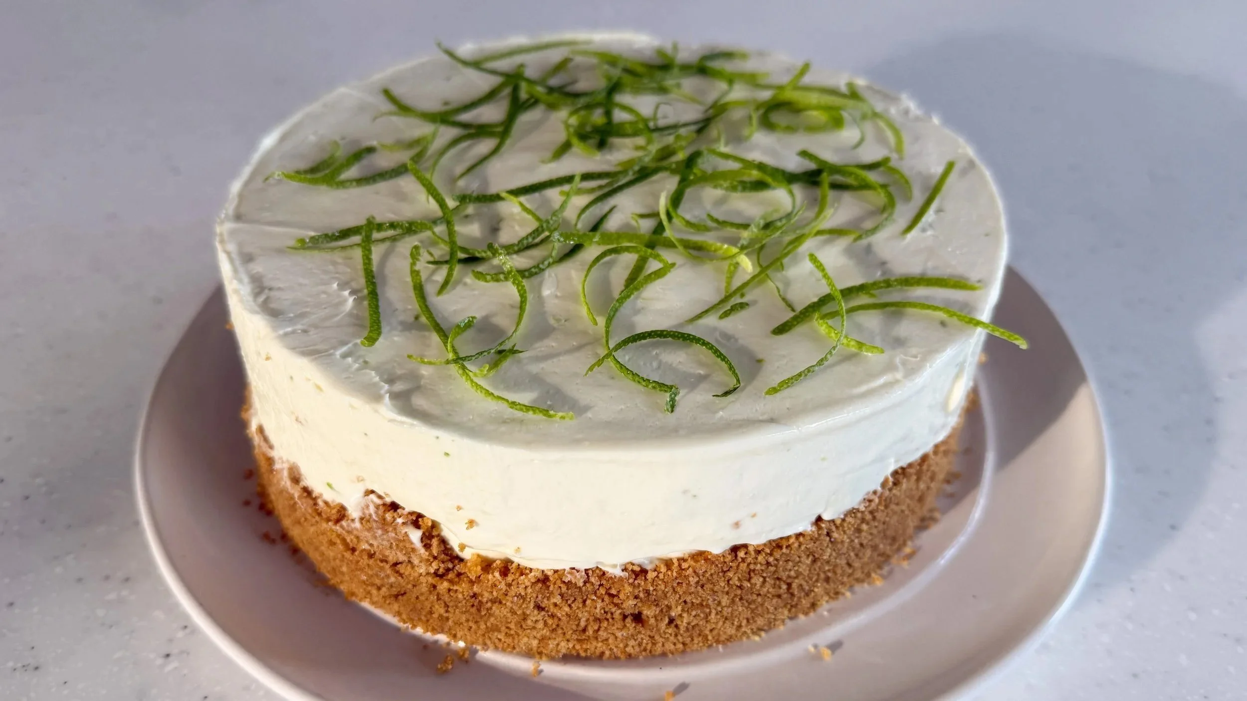 A cheesecake topped with lime zest strips sits on a white platter.