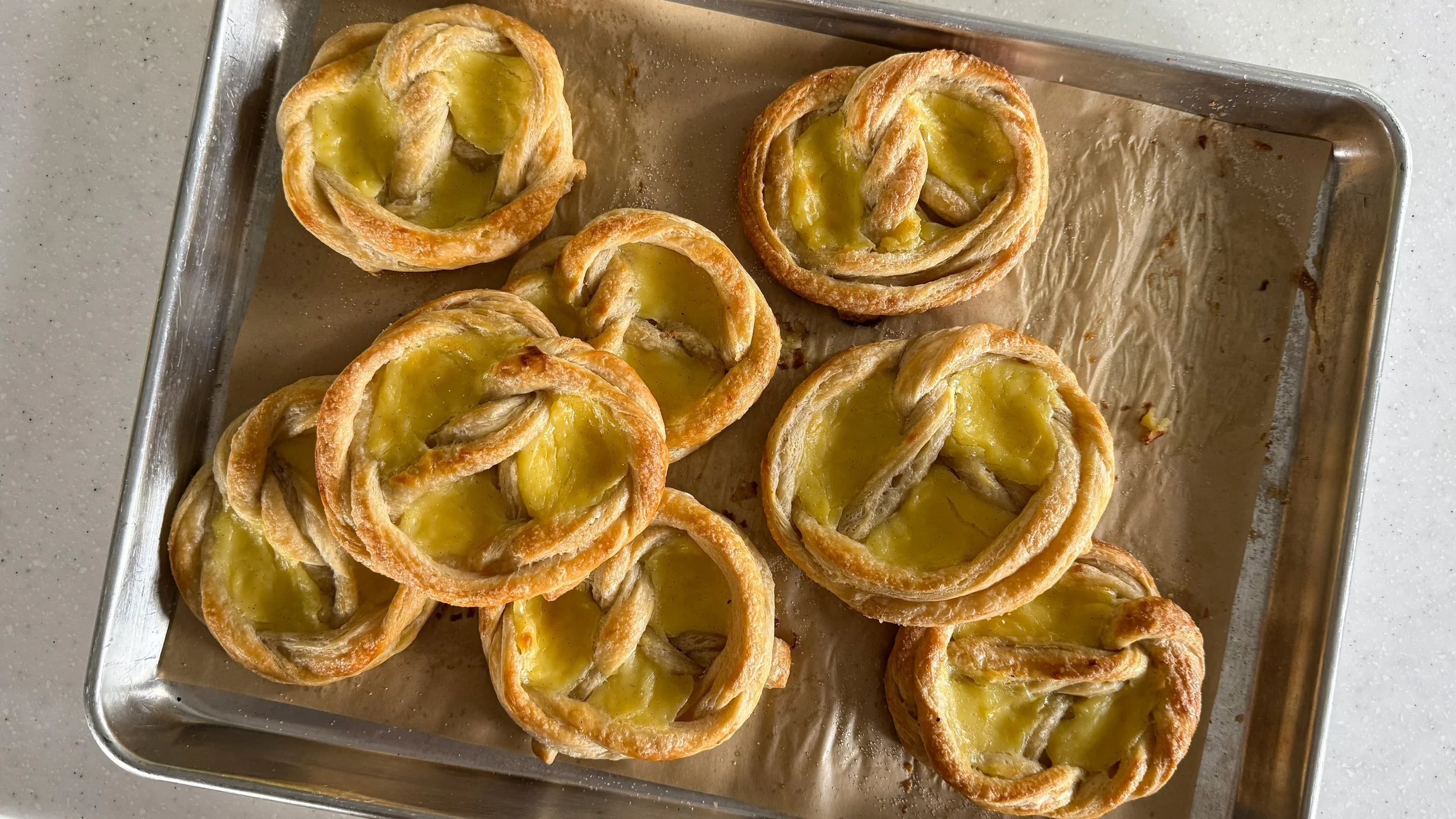 Pretzel shaped custard filled pastries on a baking sheet lined with brown parchment paper.