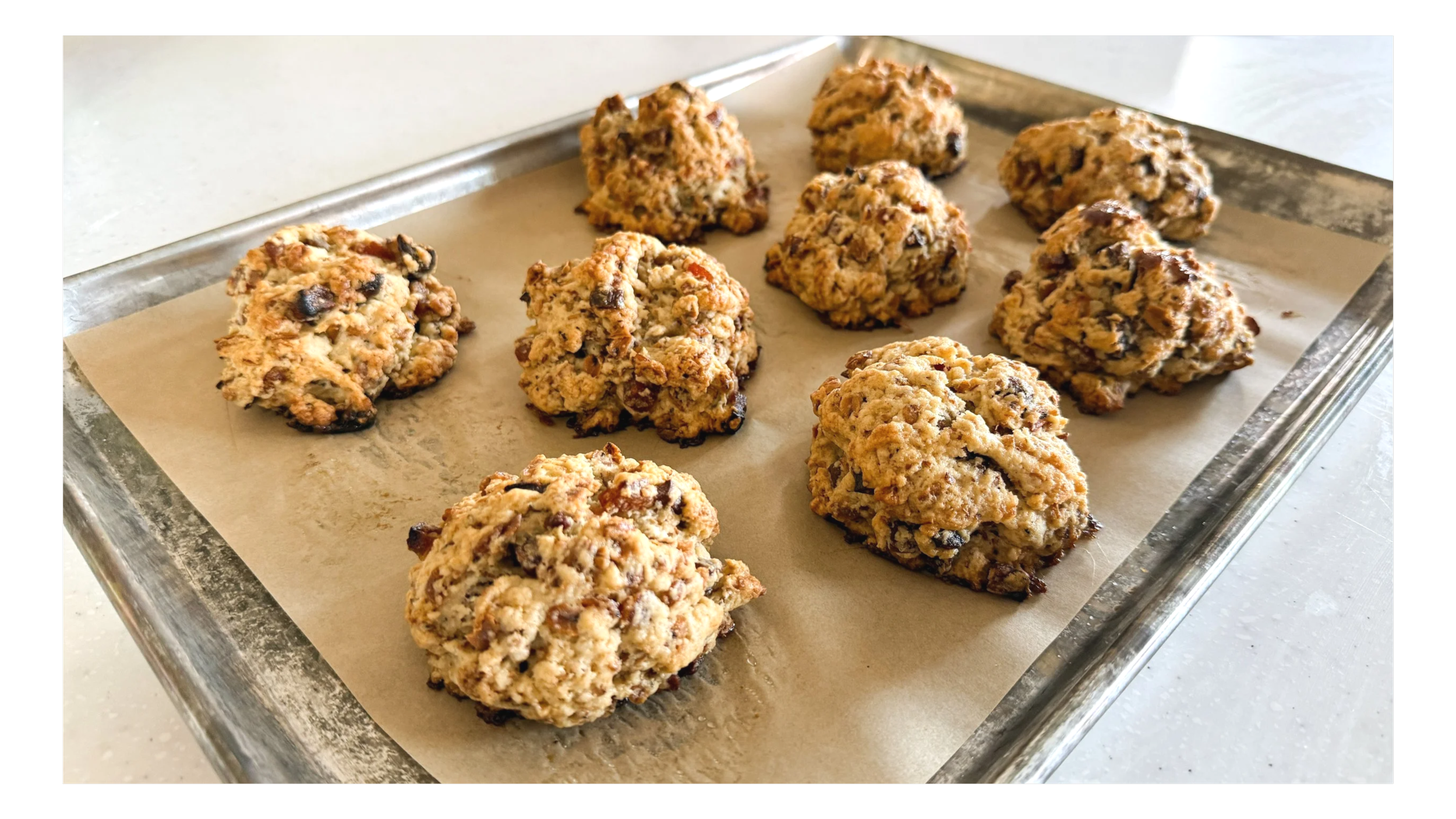 A baking sheet lined with brown parchment paper is holding 9 scones, each one contains dried apricots and toasted oats, and was glazed in maple syrup.