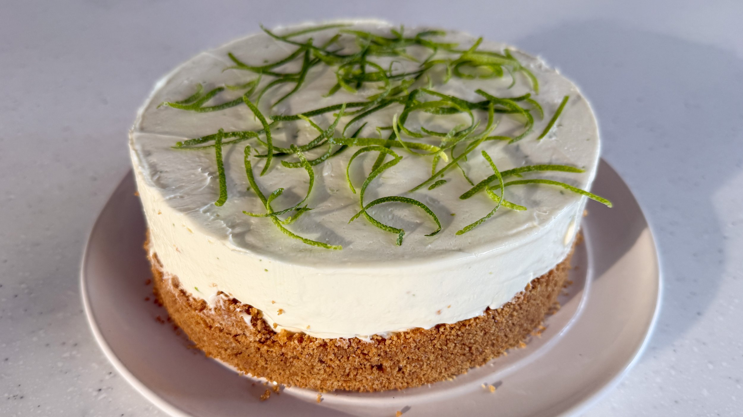 A no bake cheesecake topped with curly lime zest sits on a white serving platter.