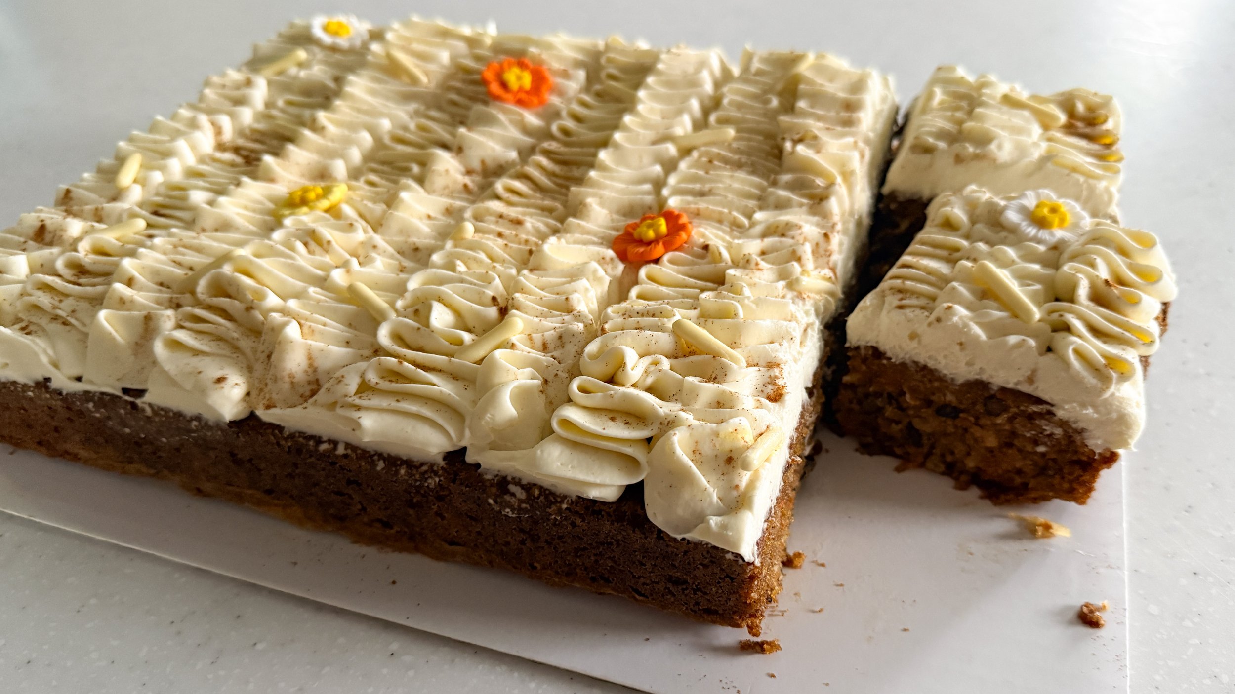 A carrot cake sheet cake on a white platter, with one slice removed and two more cut to reveal the interior crumb structure.