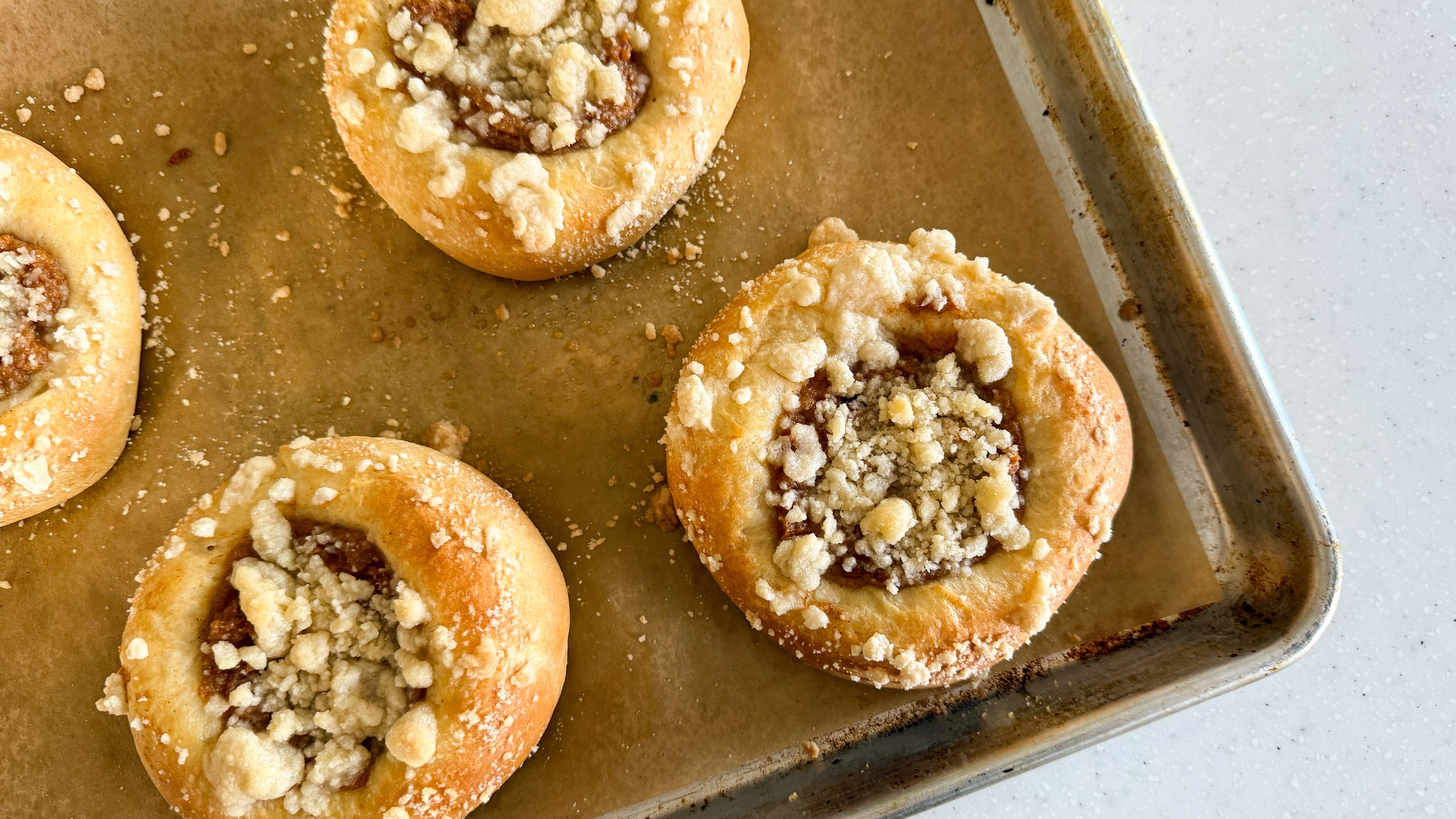 A baking sheet lined with brown parchment paper topped with crumb topped sweet potato kolache.