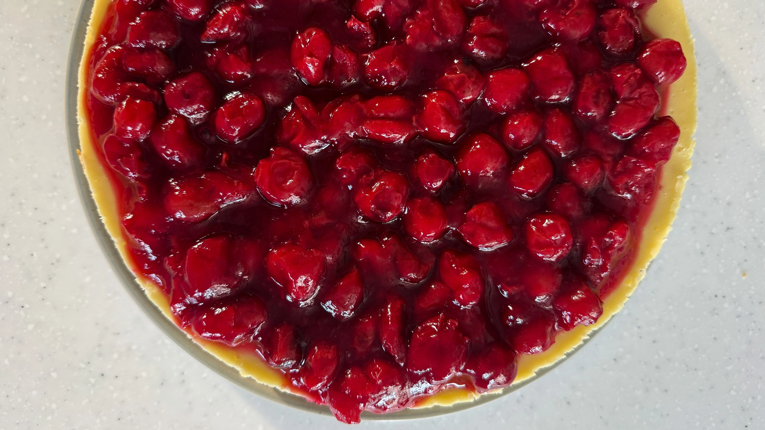 A cheesecake topped with bright red classic cherries is shown, photographed from above on a white surface.