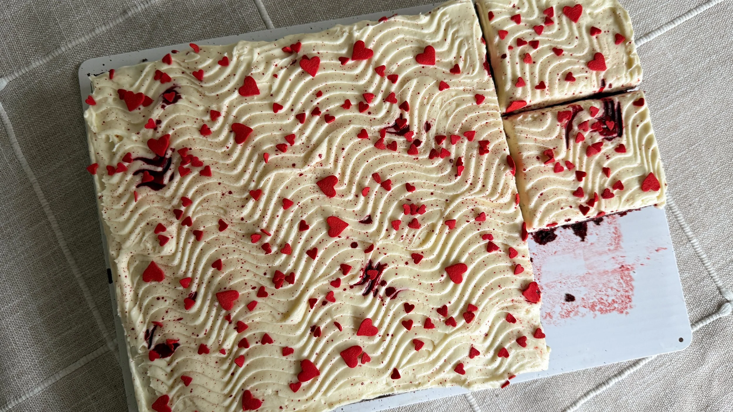 Red Velvet sheet cake with swirly cream cheese frosting and red heart sprinkles.