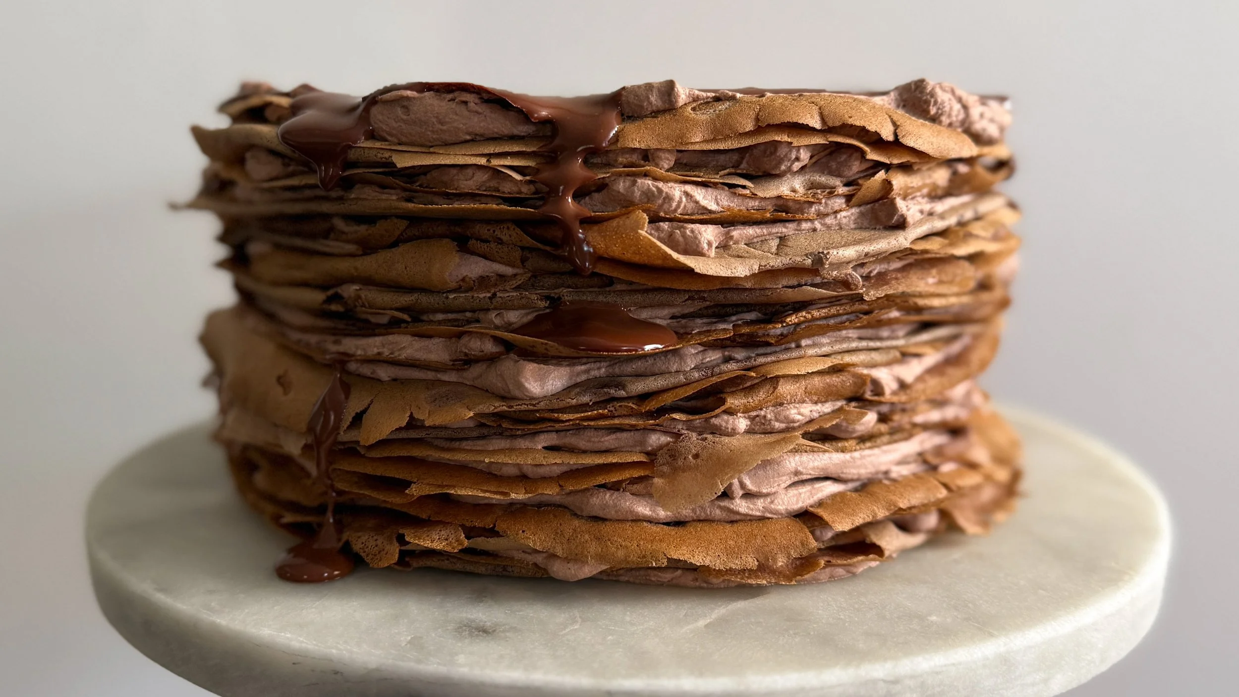 Chocolate crepes stacked with chocolate whipped cream, and topped with chocolate ganache on a marble platter