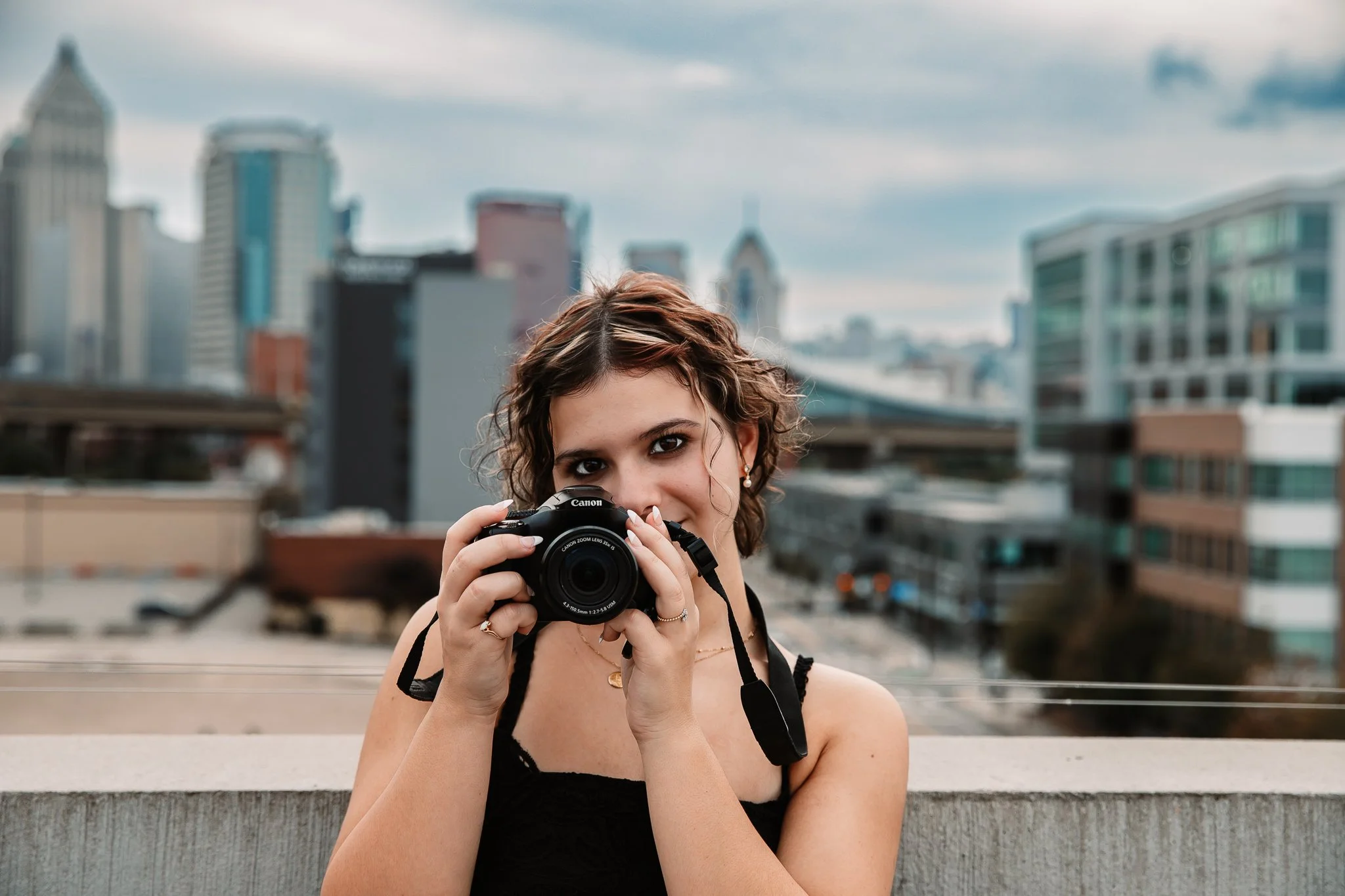 High school senior holding a camera in the Strip District with Pittsburgh skyline in the background