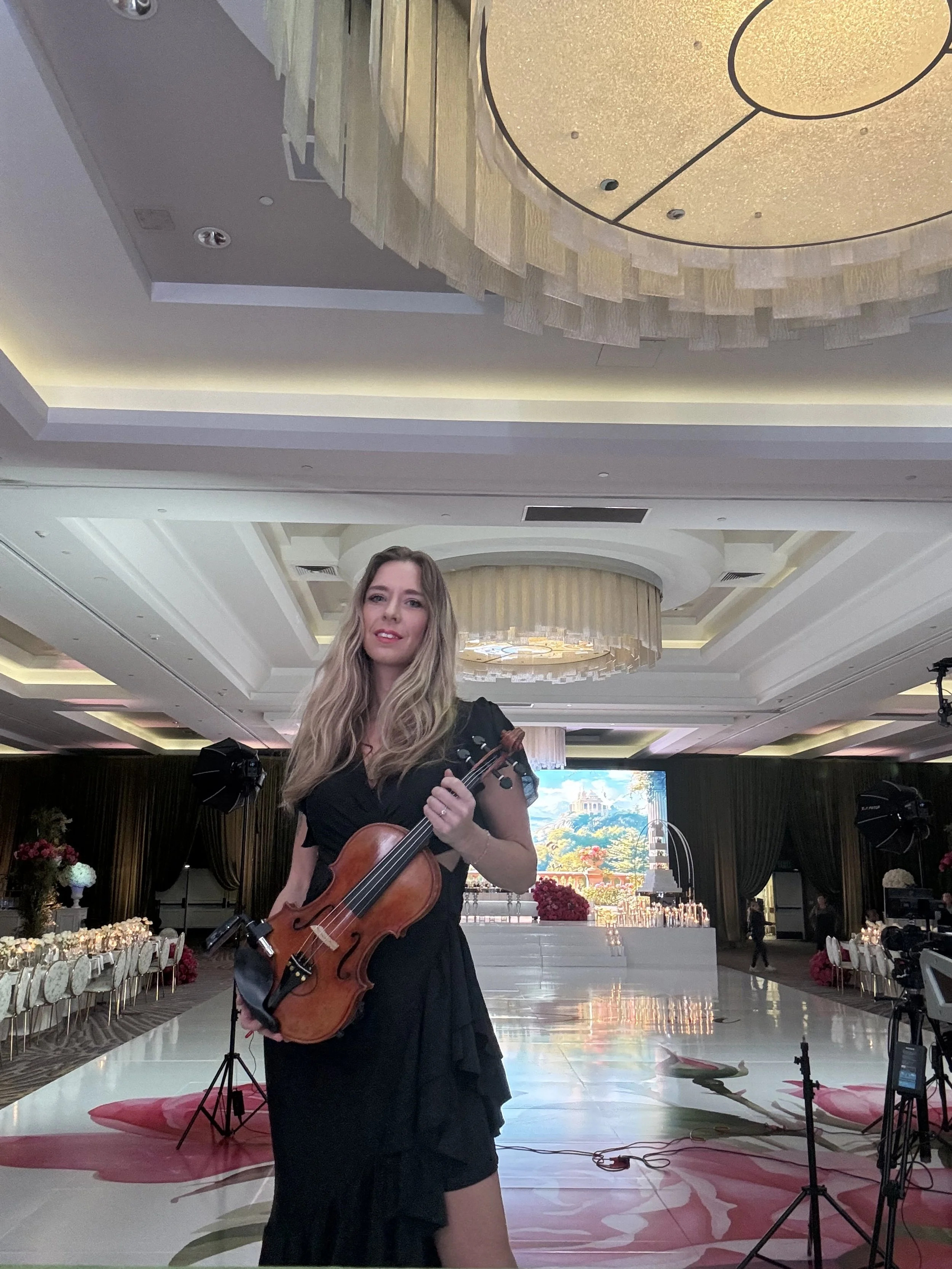 Elin Wolf in a black dress holding a violin on a decorated stage in a banquet hall.