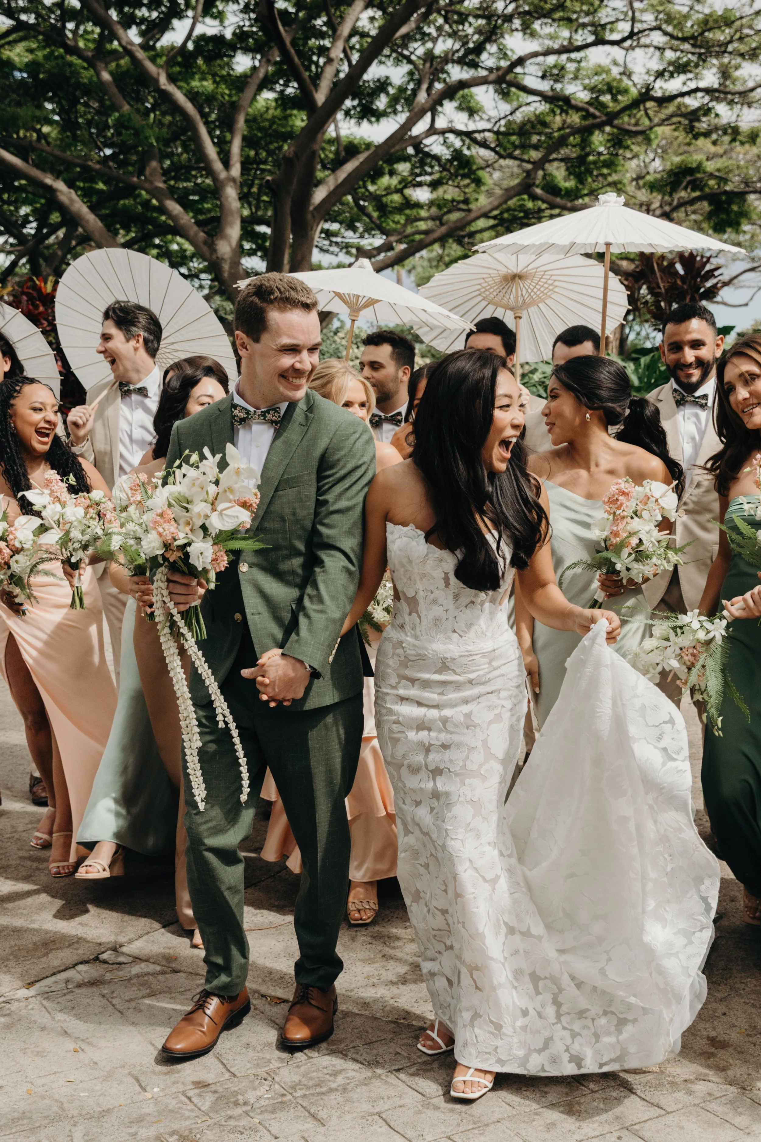 Joyful bride and groom walking with wedding guests holding umbrellas during outdoor wedding celebration.