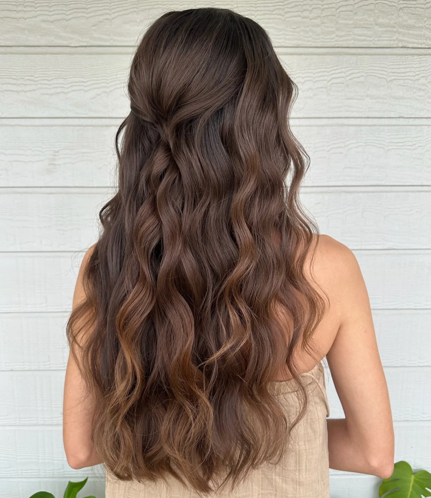 Back view of a woman with long, wavy, brown hair over a light-colored, textured wall background.