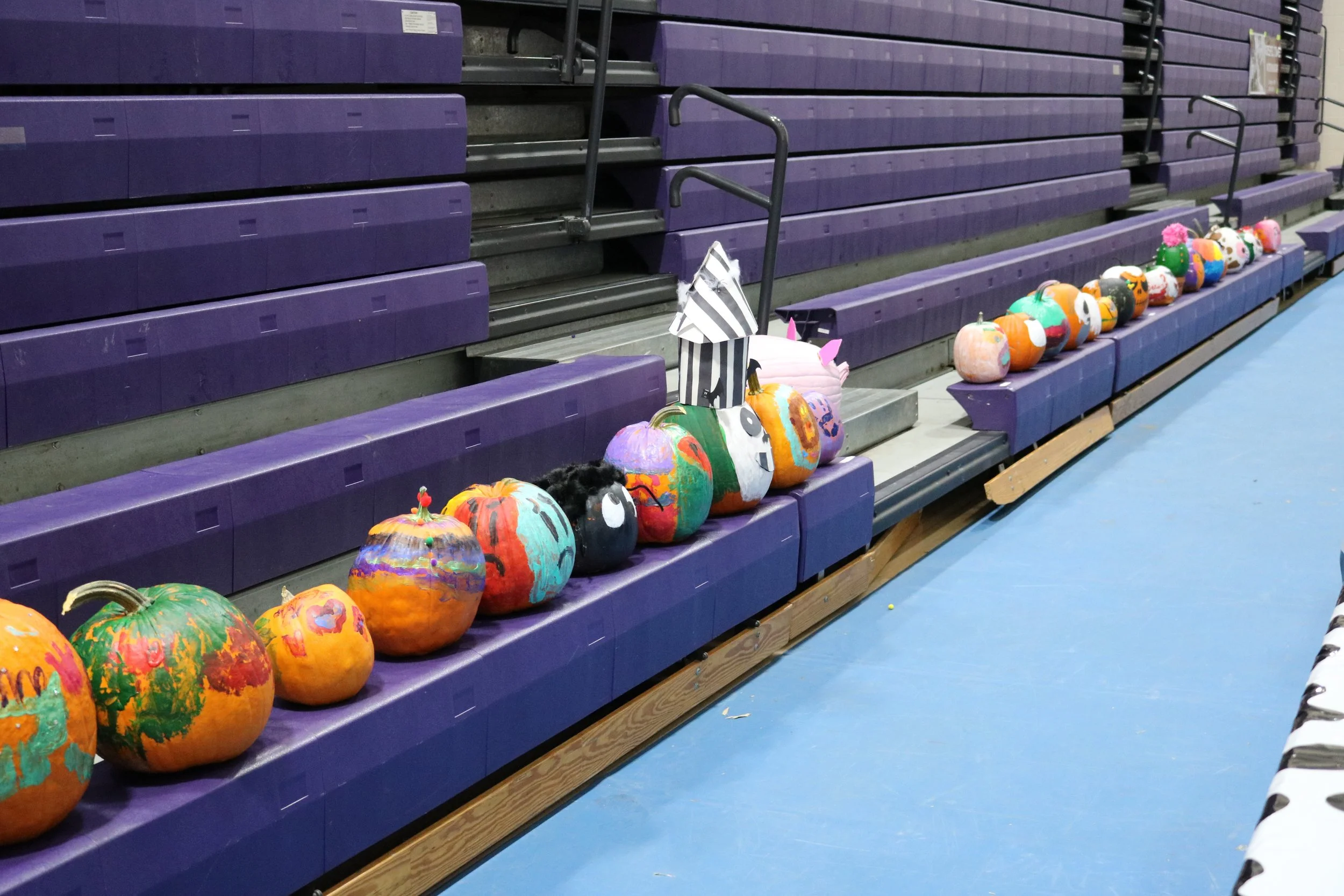 Colorfully painted pumpkins arranged on gymnasium bleachers, likely part of a Halloween or fall display.