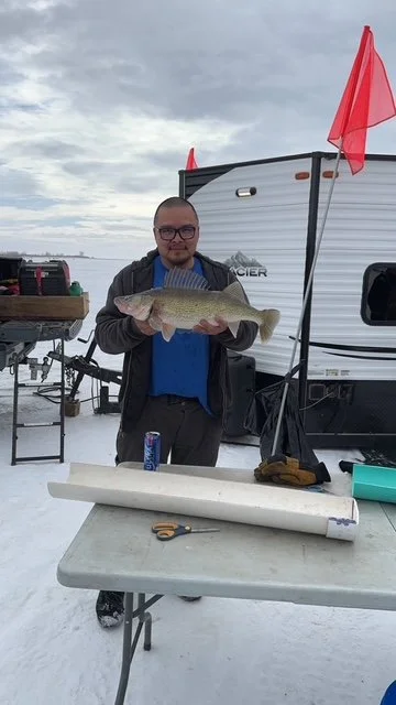 Man holding a large fish in front of a camper on a snowy day
