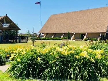 A garden with yellow flowers in front of a building with a brown roof and an American flag on a flagpole.
