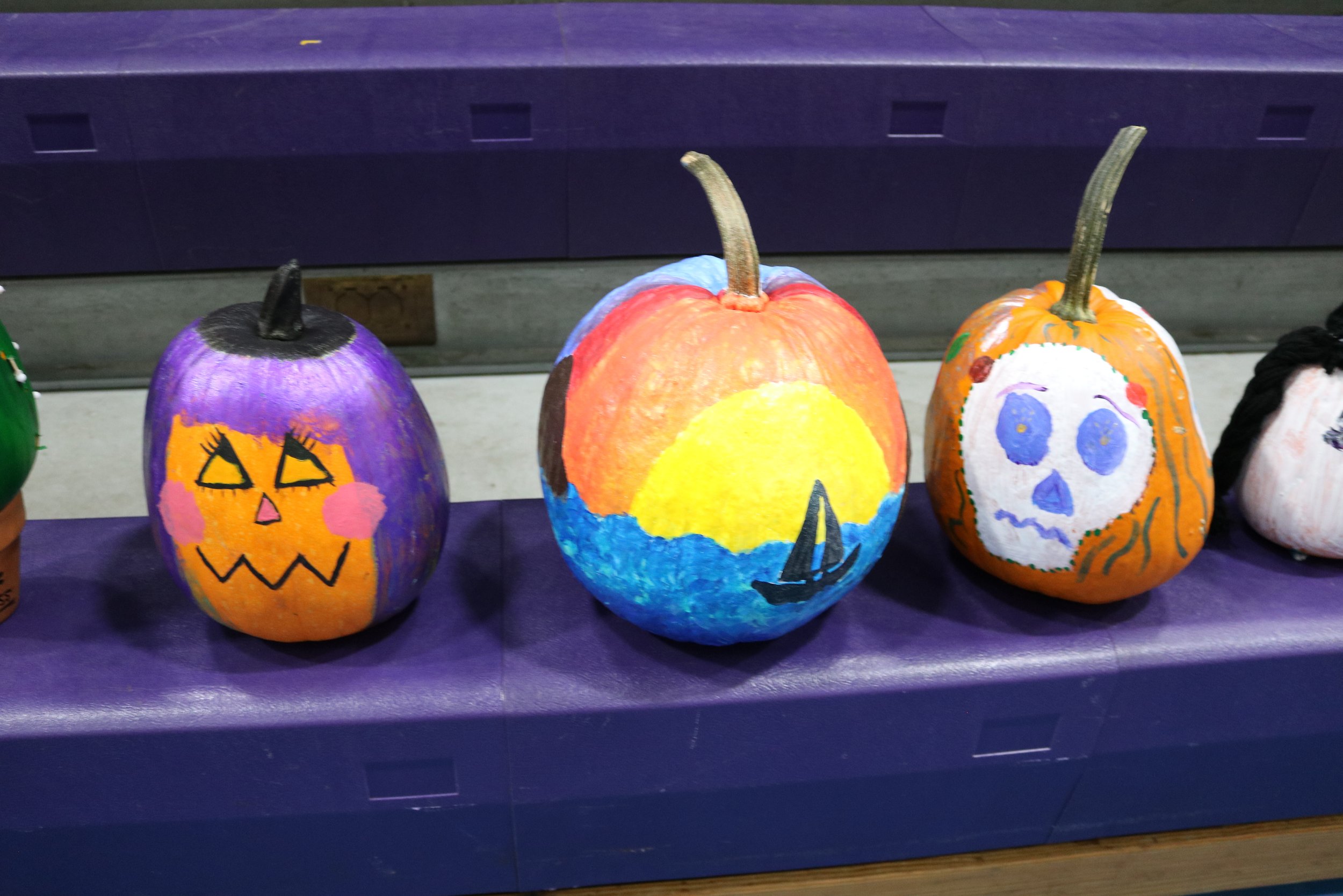 Three decorated pumpkins with Halloween and autumn designs on a purple table.