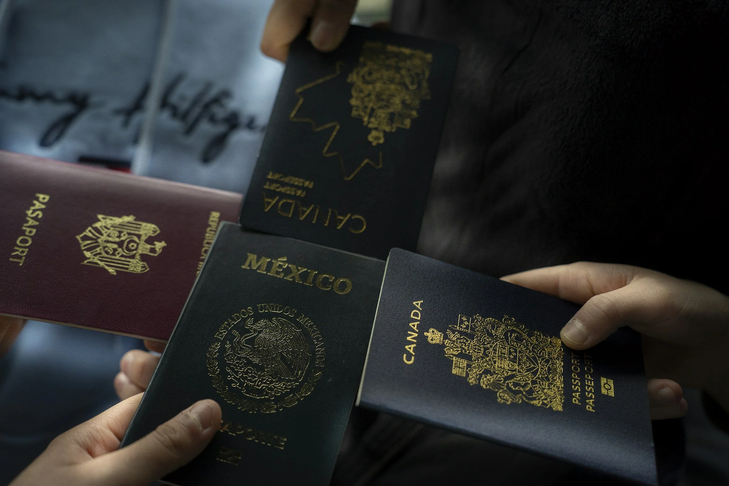 Several passports from different countries, including Canada and Mexico, are being held by hands against a blurred background.