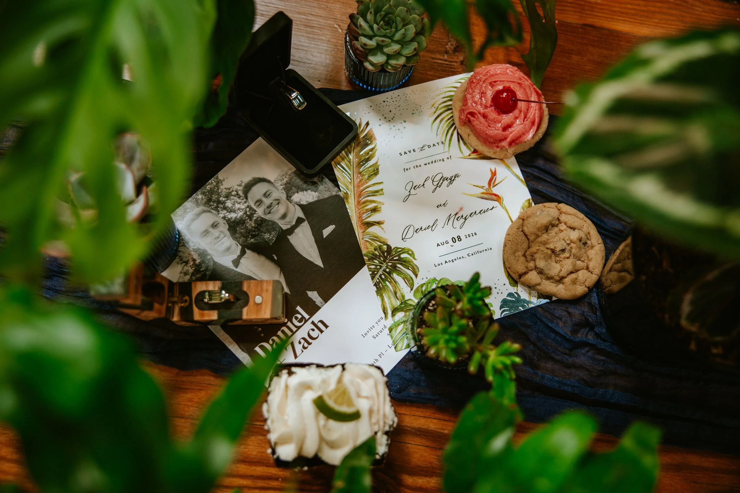 Close up of wedding invitation flatlay featuring wedding rings and Crumbl cookies