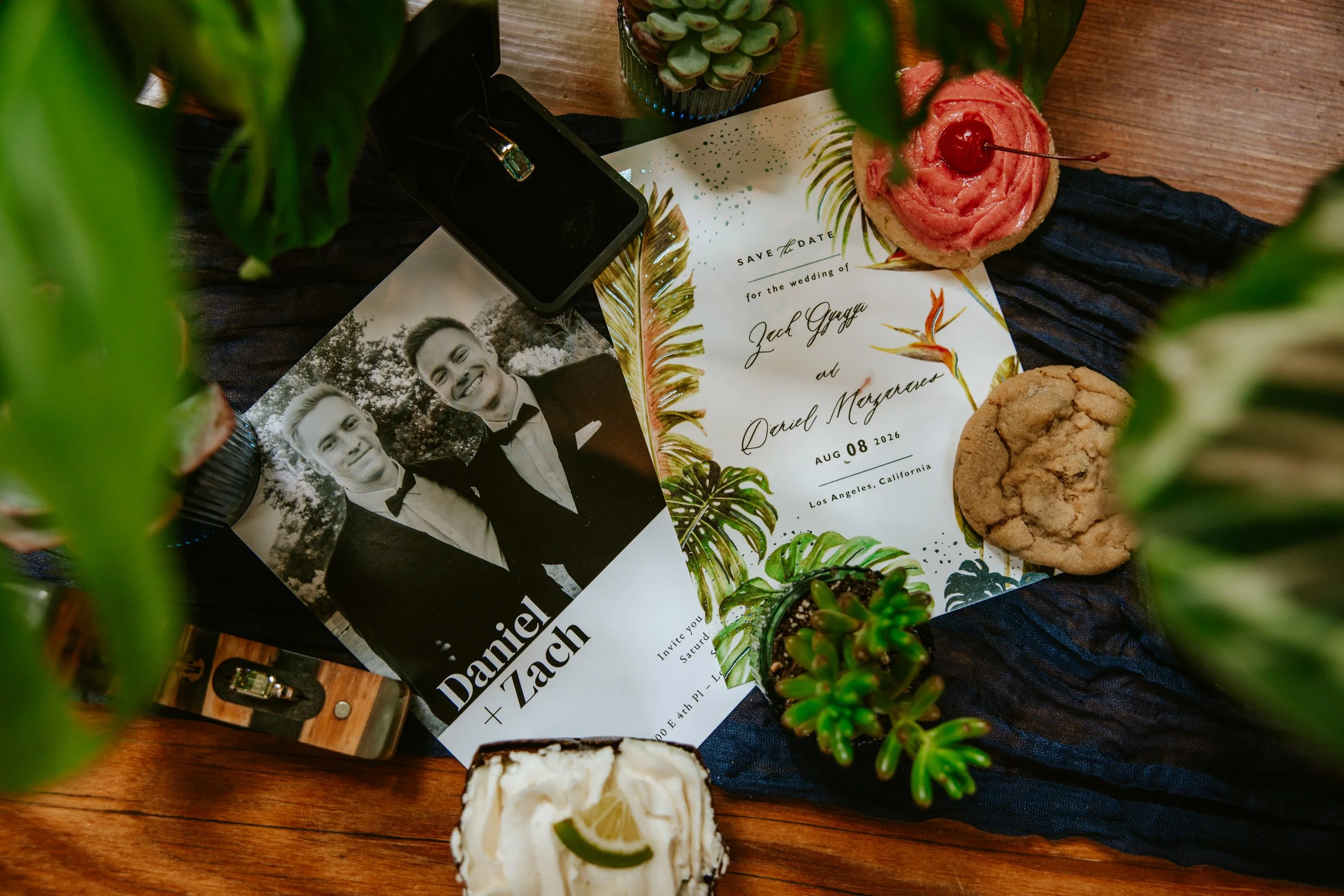 Wedding invitation flatlay featuring wedding rings and Crumbl cookies