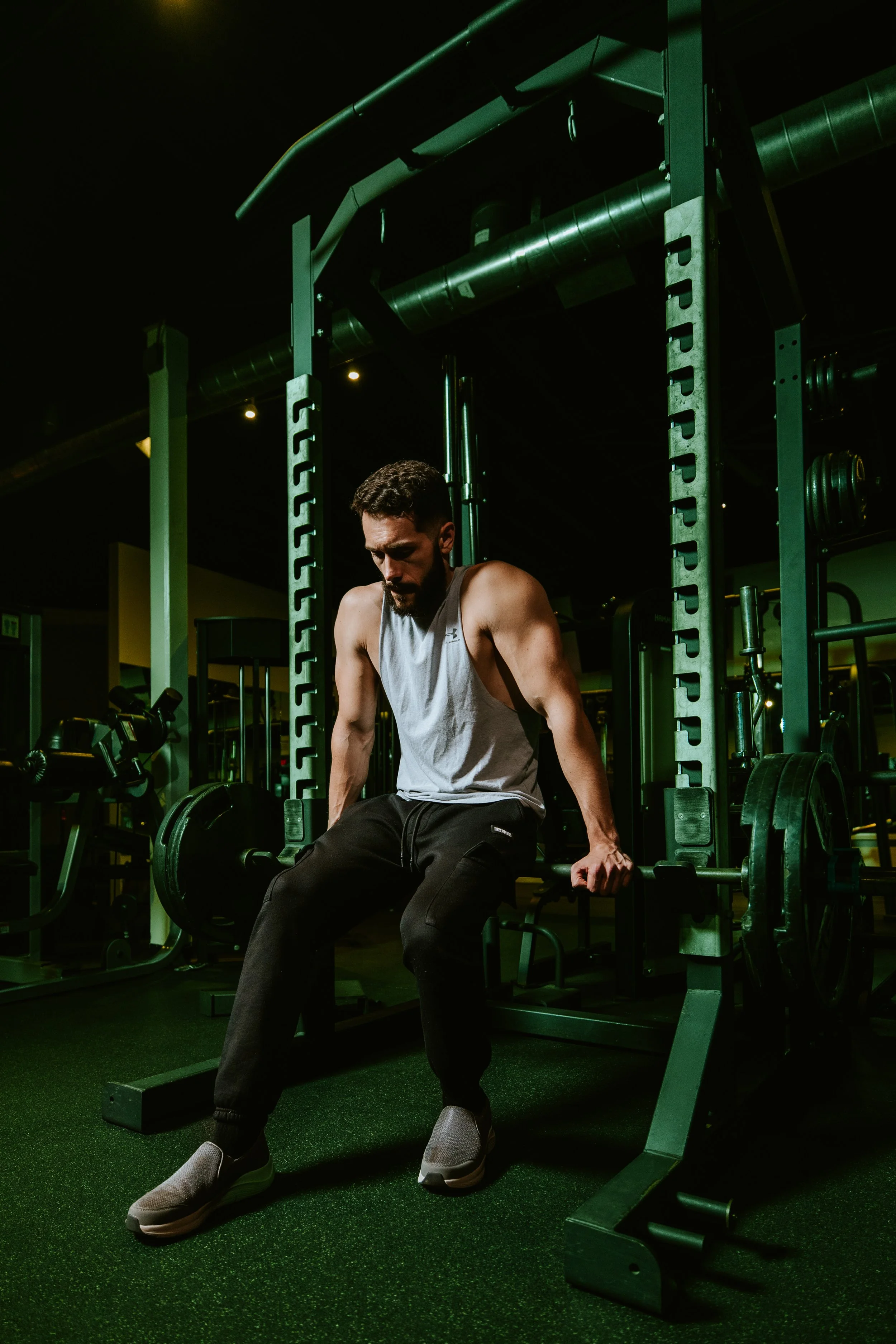 A man sitting on a workout bench in a gym, dressed in workout clothes, with weights and gym equipment around him.