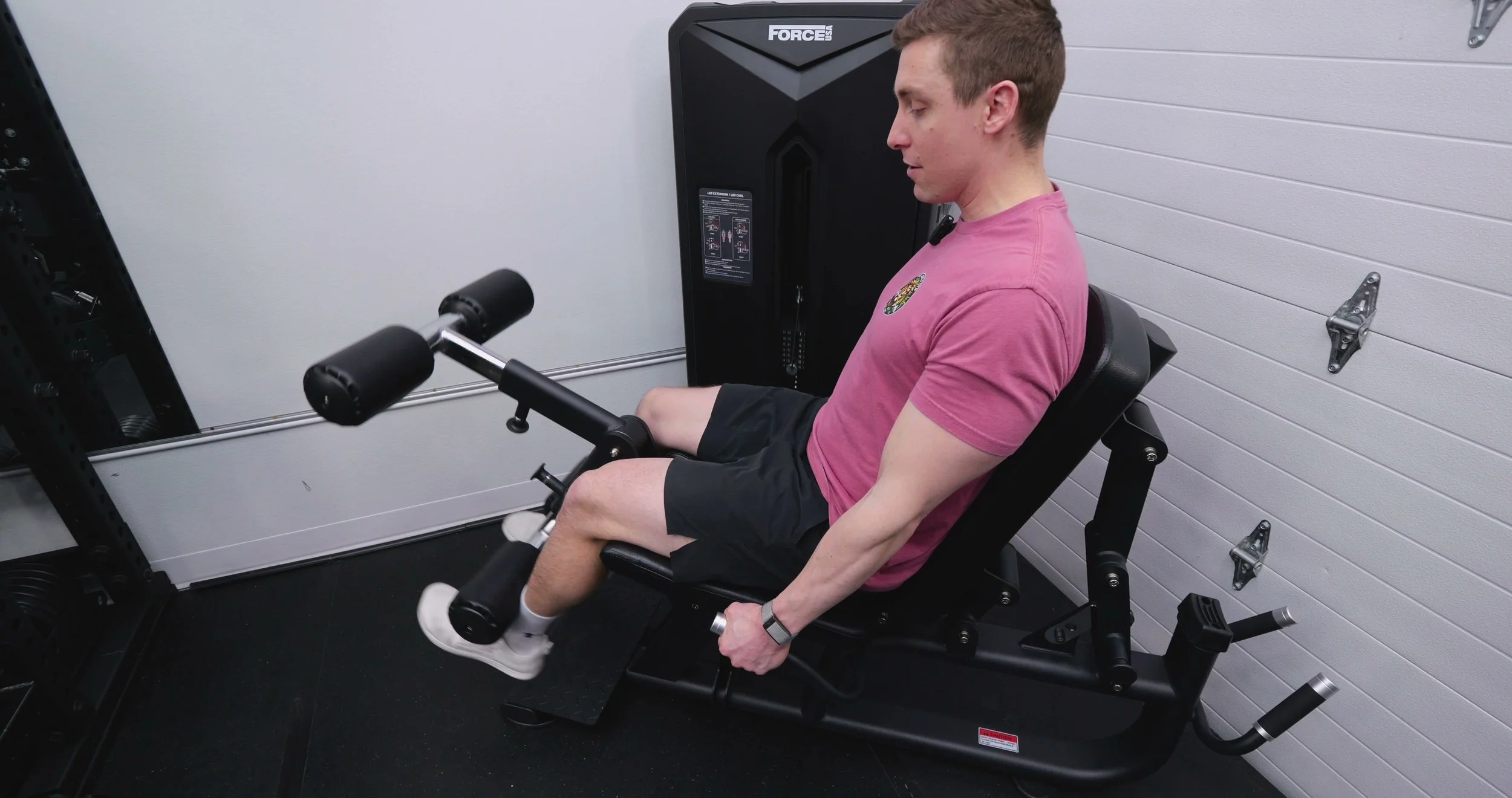 Performing a seated leg extension on the Force USA Solitude showing the center-driven cable and pad position
