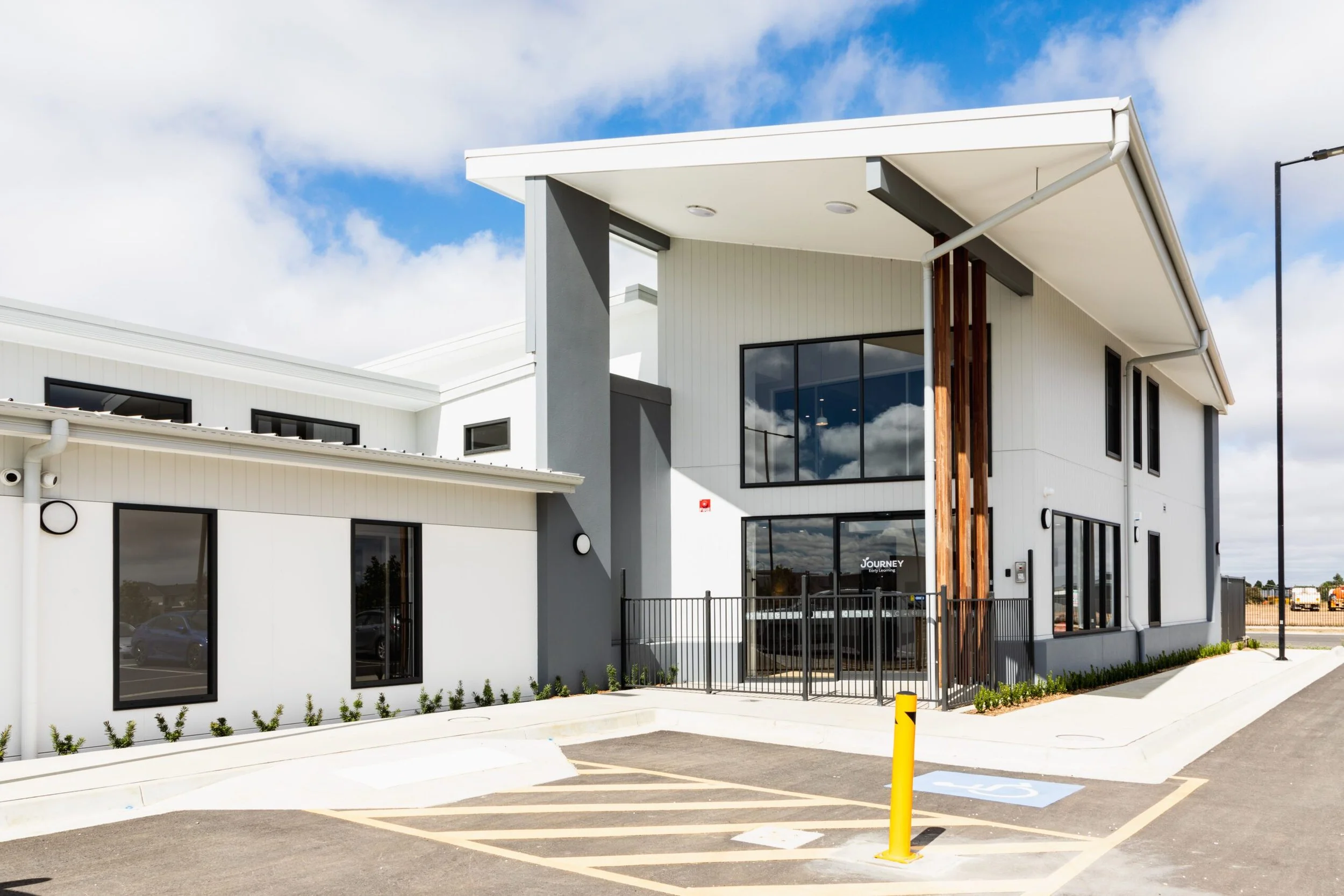 Modern commercial building with large glass windows, metal and wooden accents, and a parking lot with a designated handicapped space.