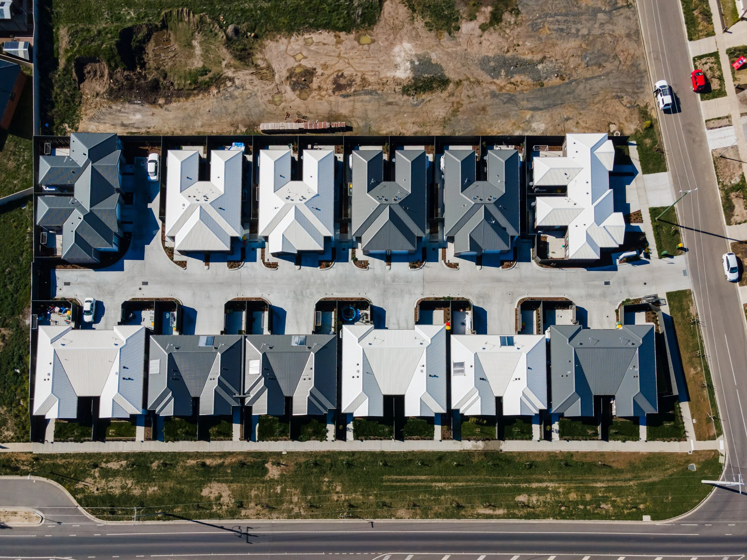Aerial view of a residential complex with multiple townhouses, parking spaces, and surrounding streets, with some construction or bare ground at the top.