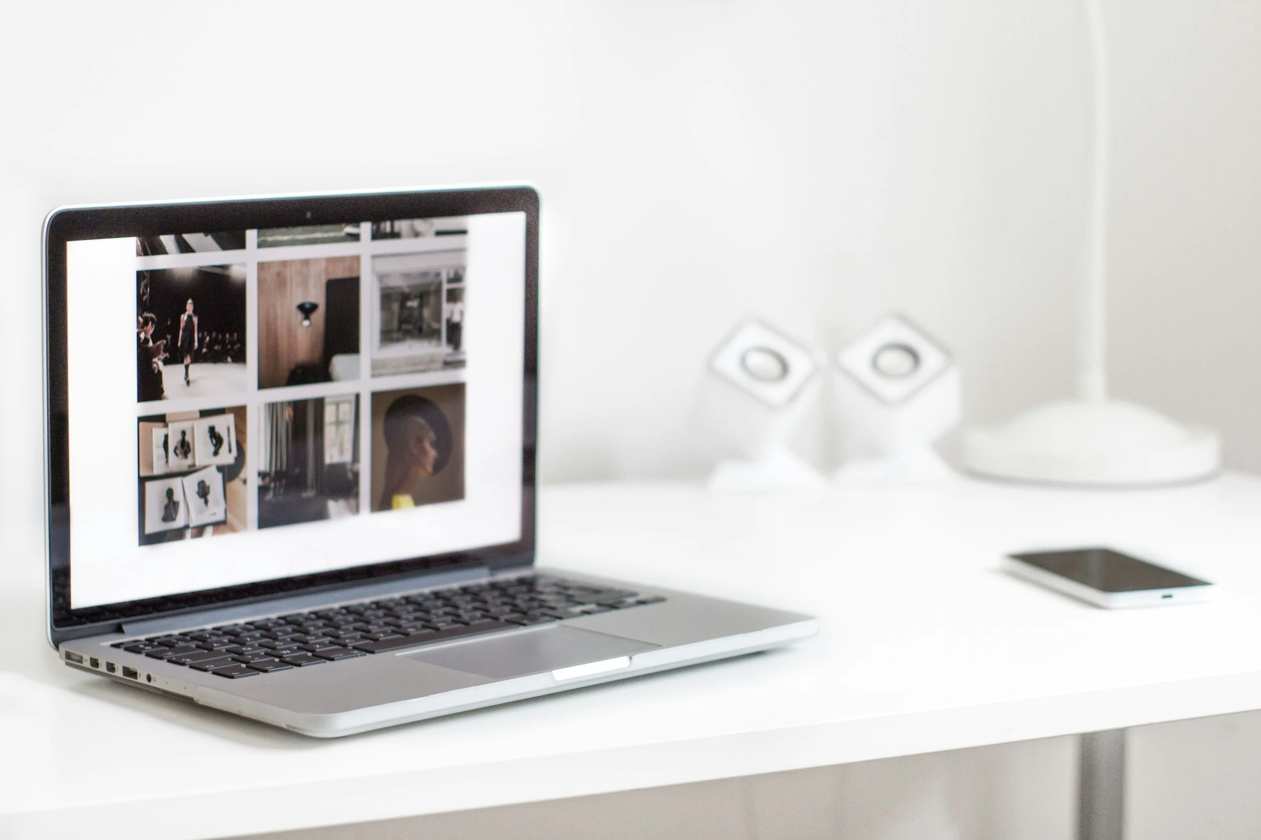 Laptop computer on white desk displaying an online photo gallery, with a portion of a silver external hard drive visible in the background. Virtual assistant for service-based businesses.