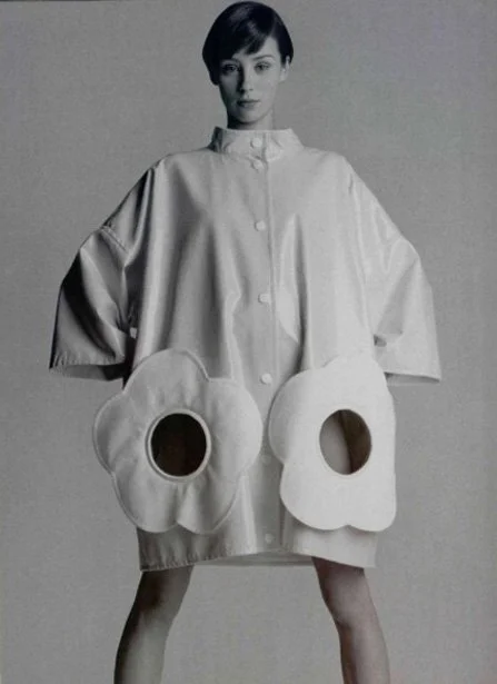 A woman wearing a large, oversized coat with big flower-shaped pockets.