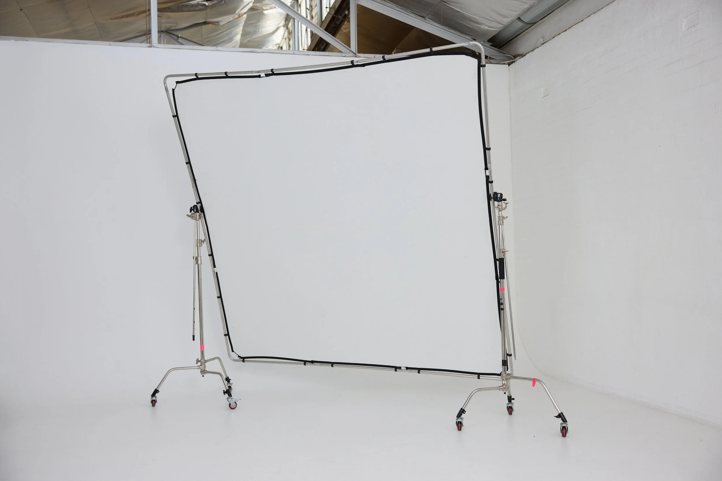 Photo of a photography scrim and stand with a white backdrop, set up in a photography studio.