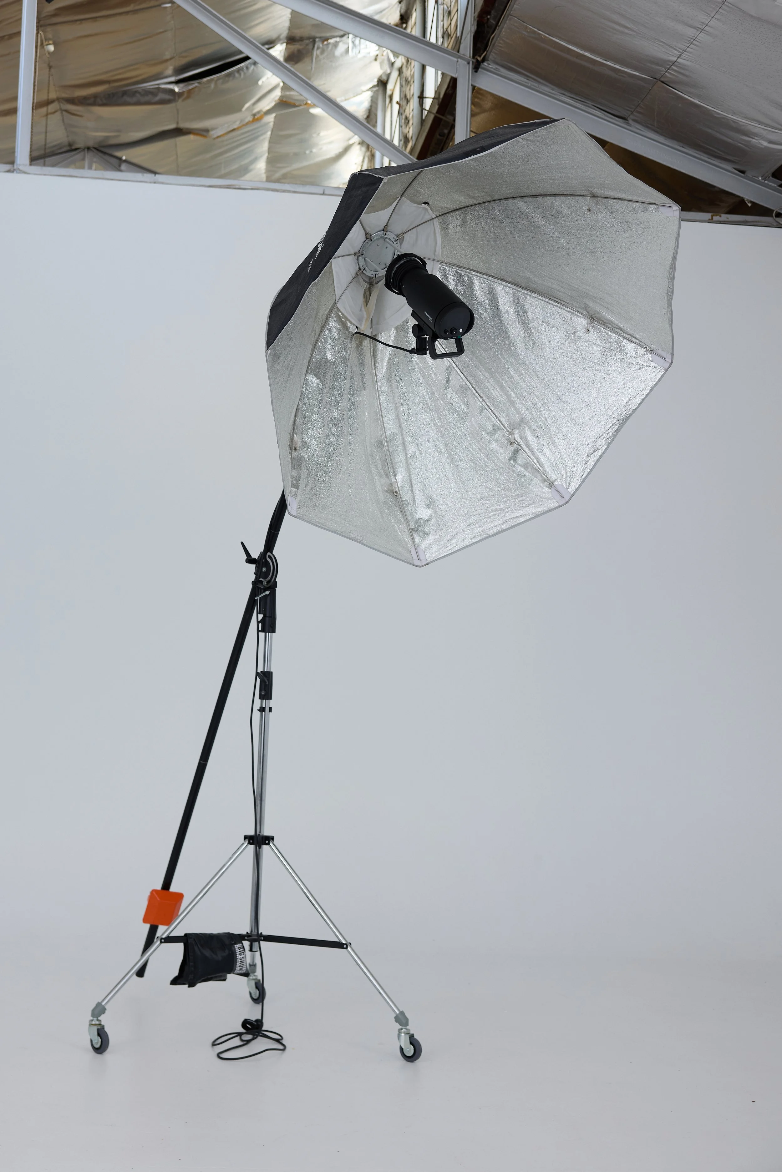 Photography studio setup with a large umbrella light reflector on a wheeled stand against a plain white background.